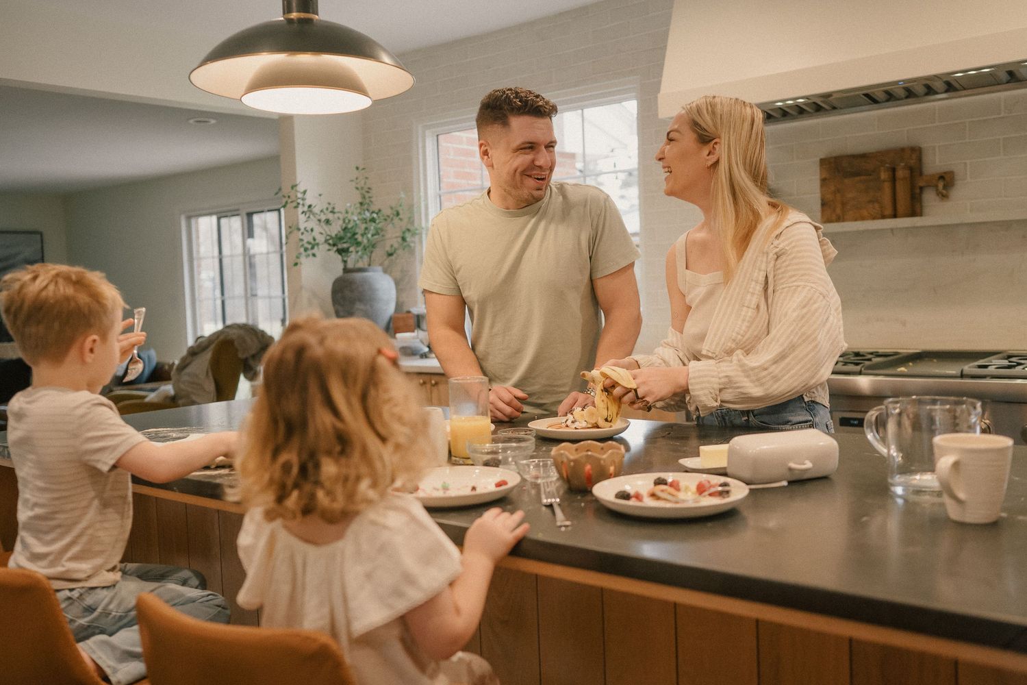 Family enjoying breakfast together in a modern kitchen, parents and two young children sharing a meal at the counter.
