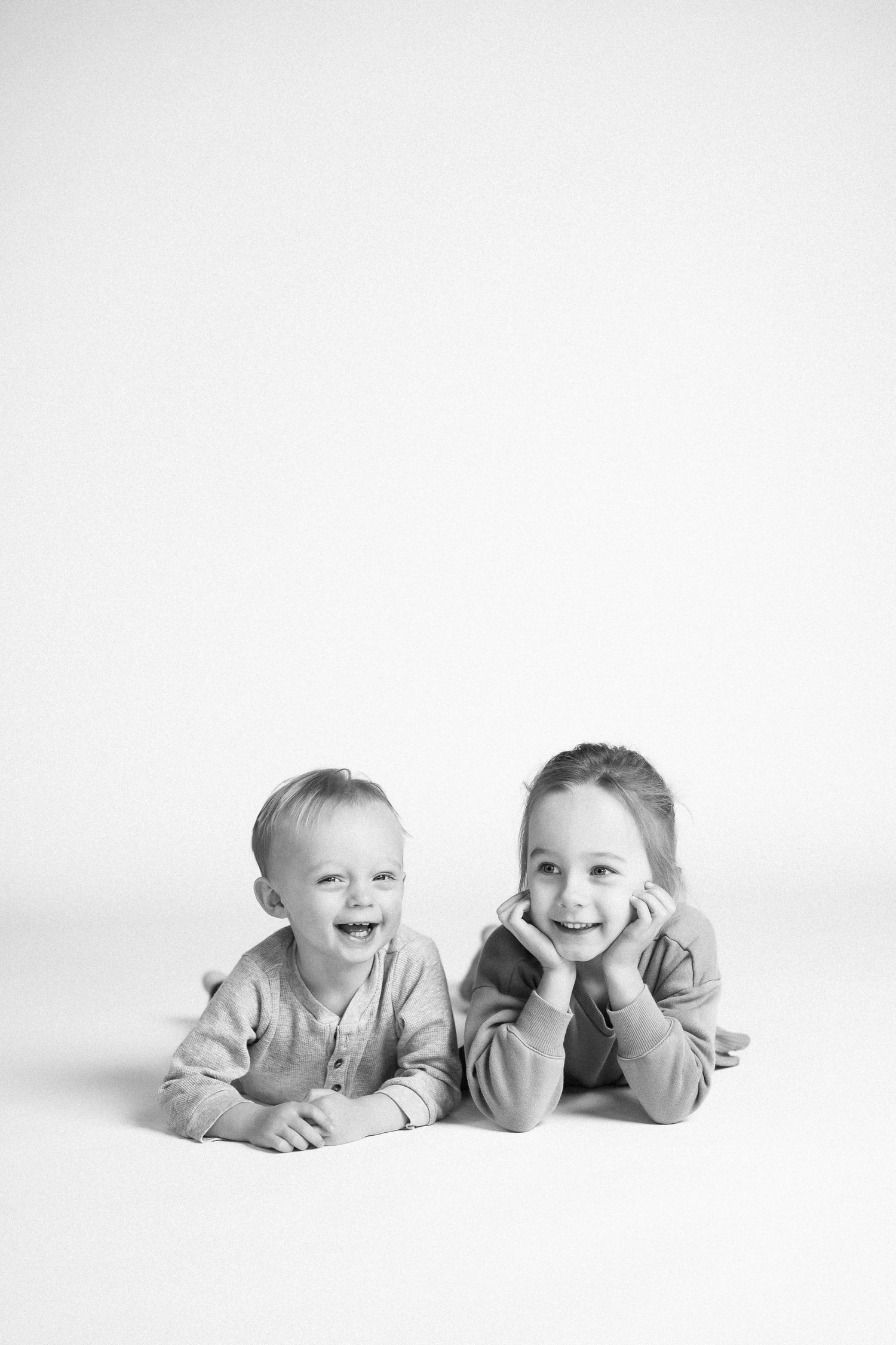 Black and white photo of babies lying on their stomachs in a row, smiling and laughing together.