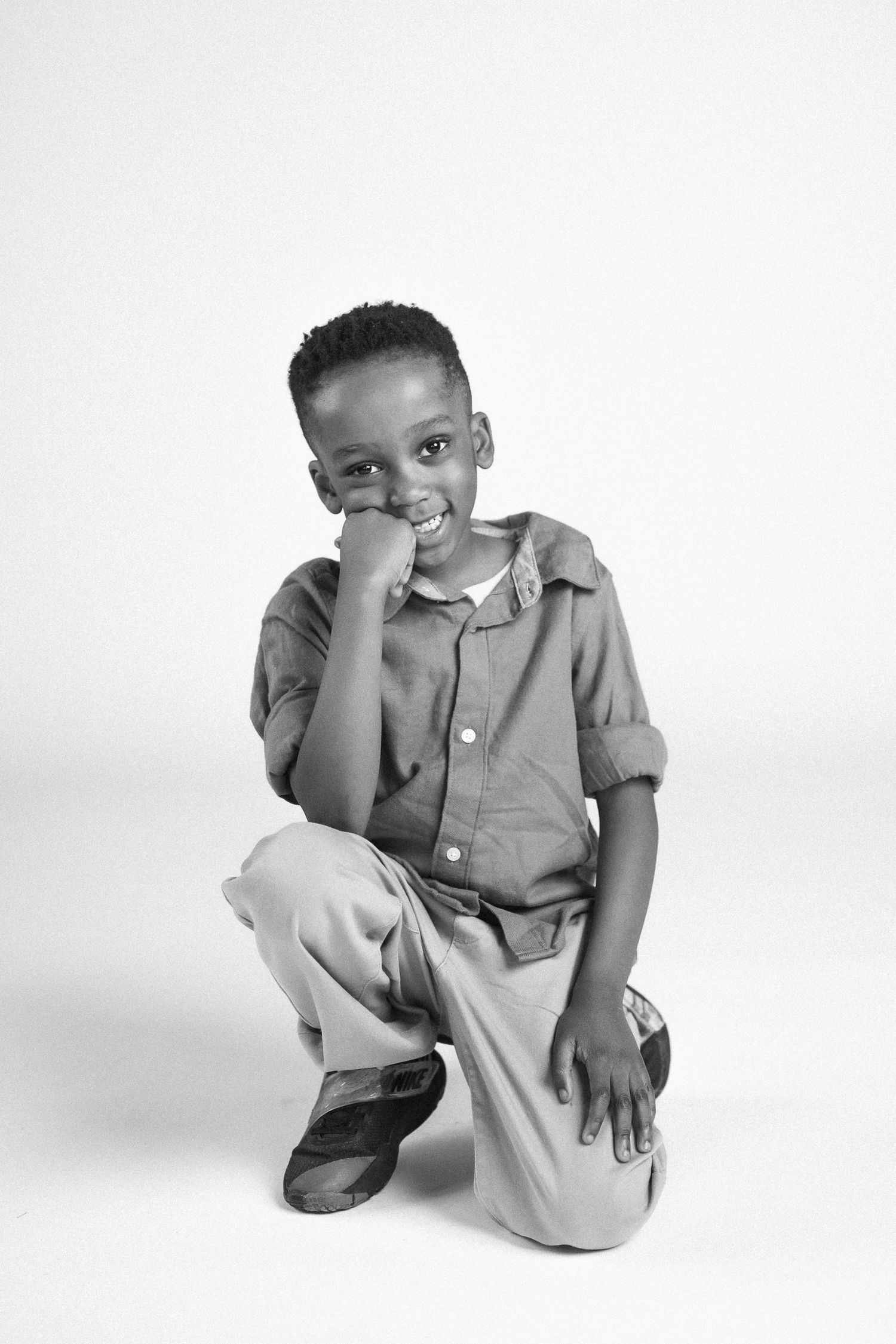 A child crouches down and rubs their eyes in a minimalist studio setting.