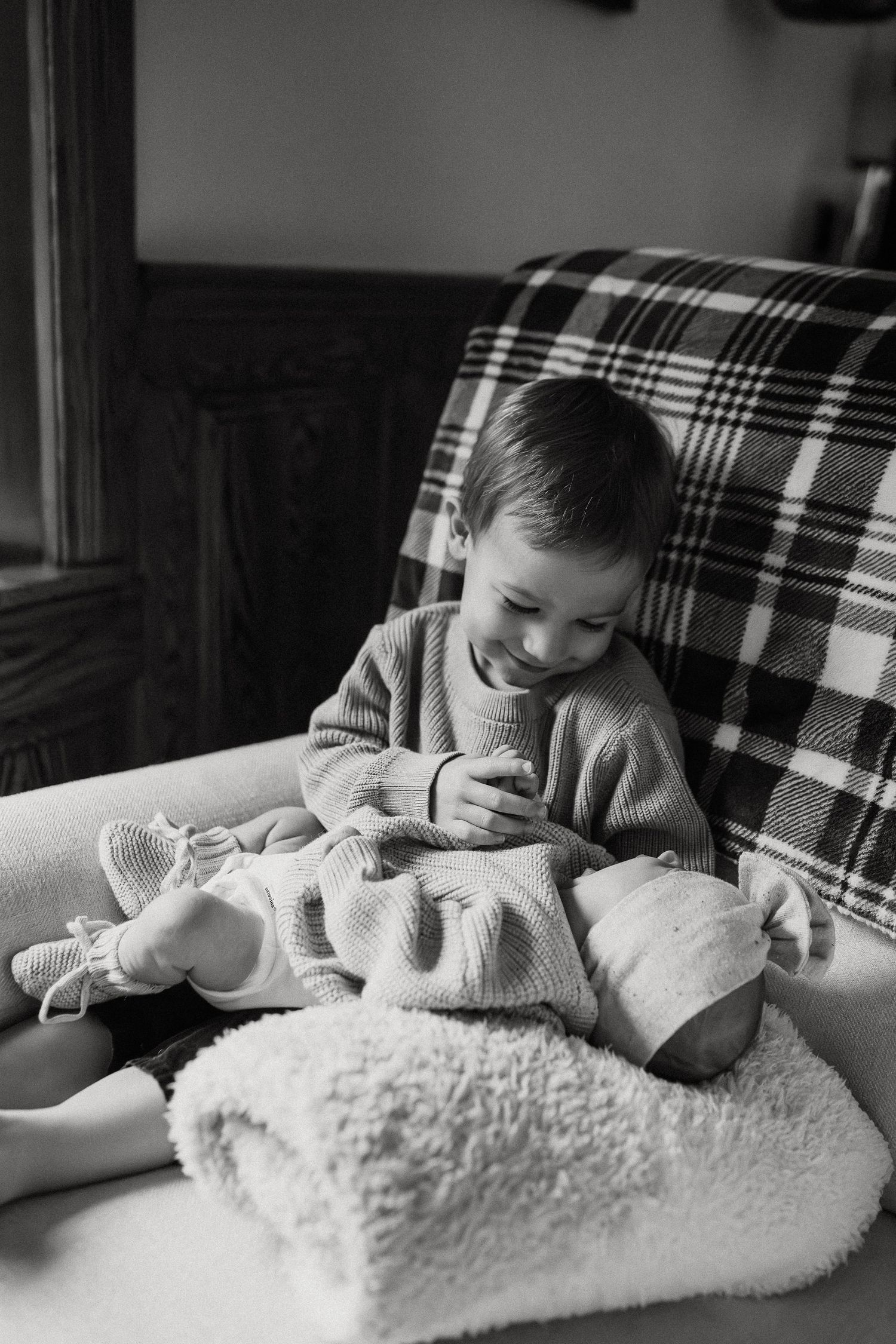 A young child in a white sweater cuddles with a plush white blanket on a plaid couch.