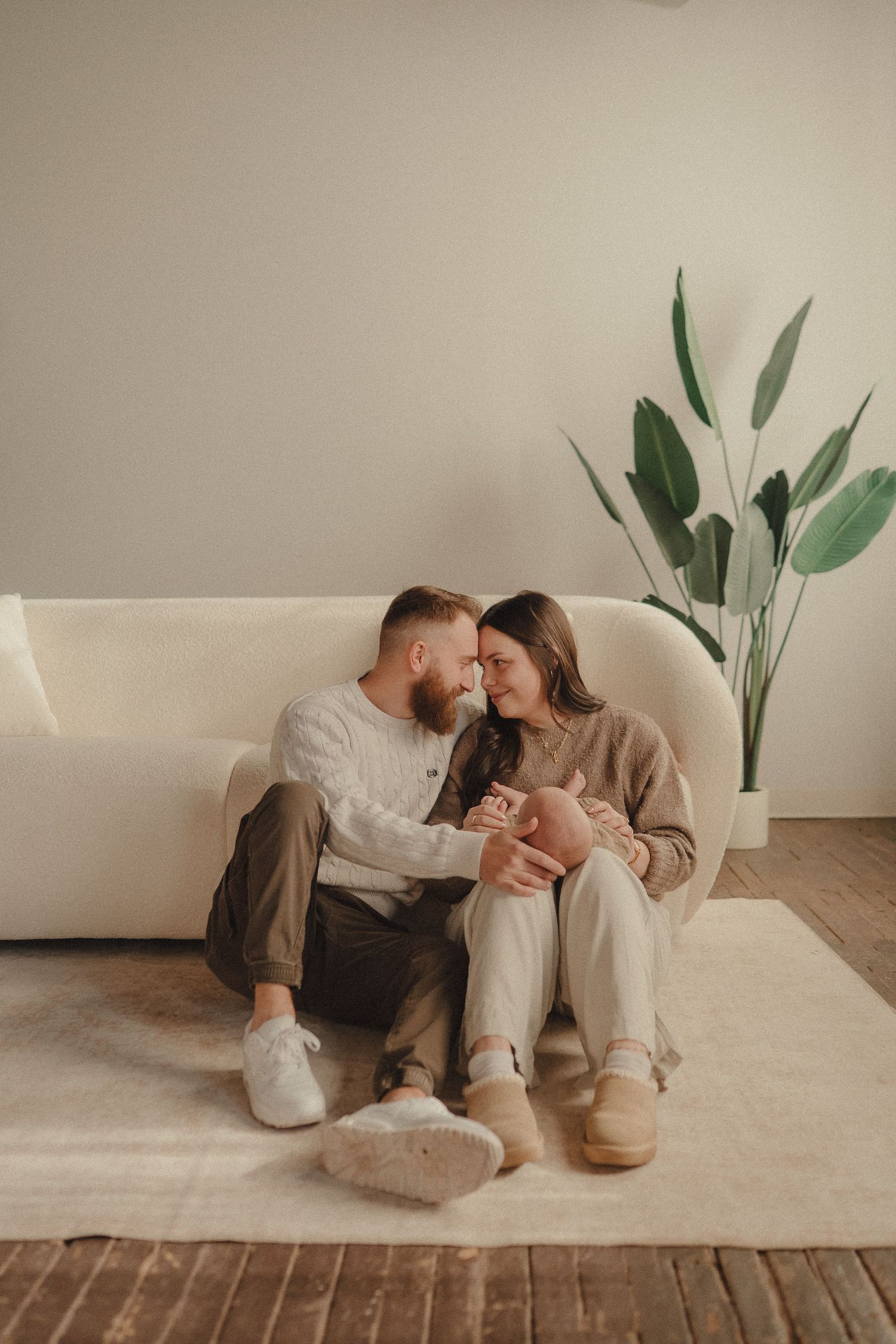 A cozy couple relaxes together on a cream colored couch with a decorative plant in the background.