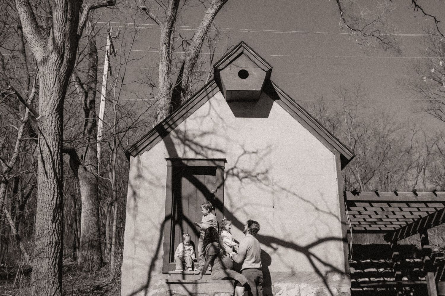 A series of playful moments captured against a small building with a birdhouse in black and white.