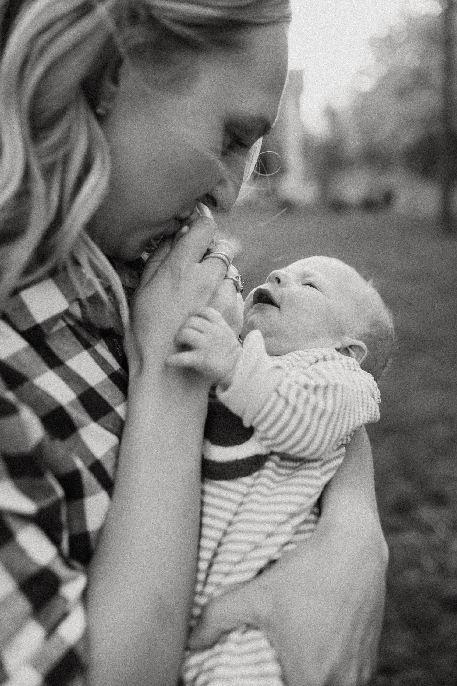 Black and white photo of a smiling mother tenderly holding her laughing newborn baby outdoors.