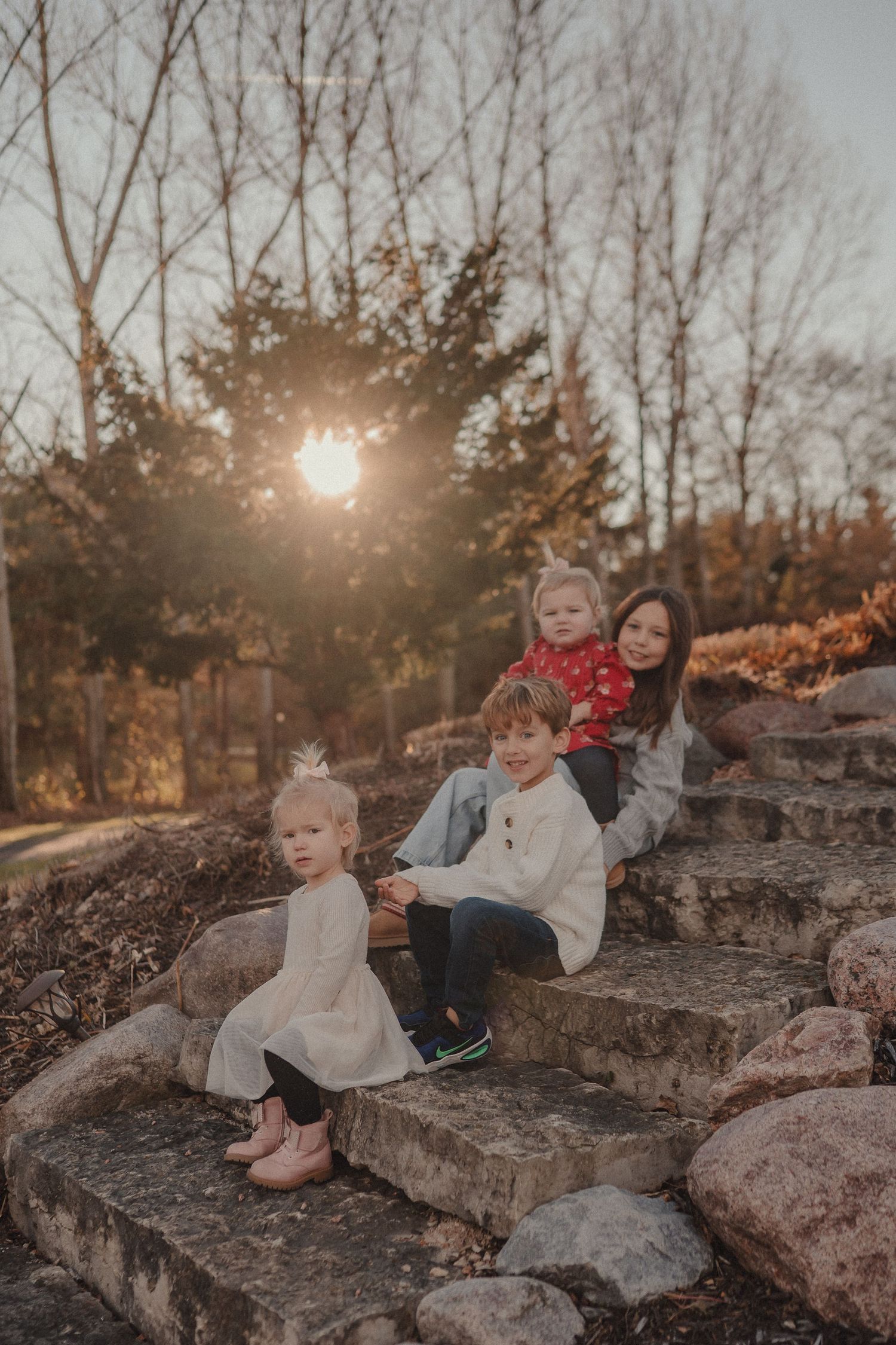 Children sitting on large rocks during golden hour with bare trees in background.