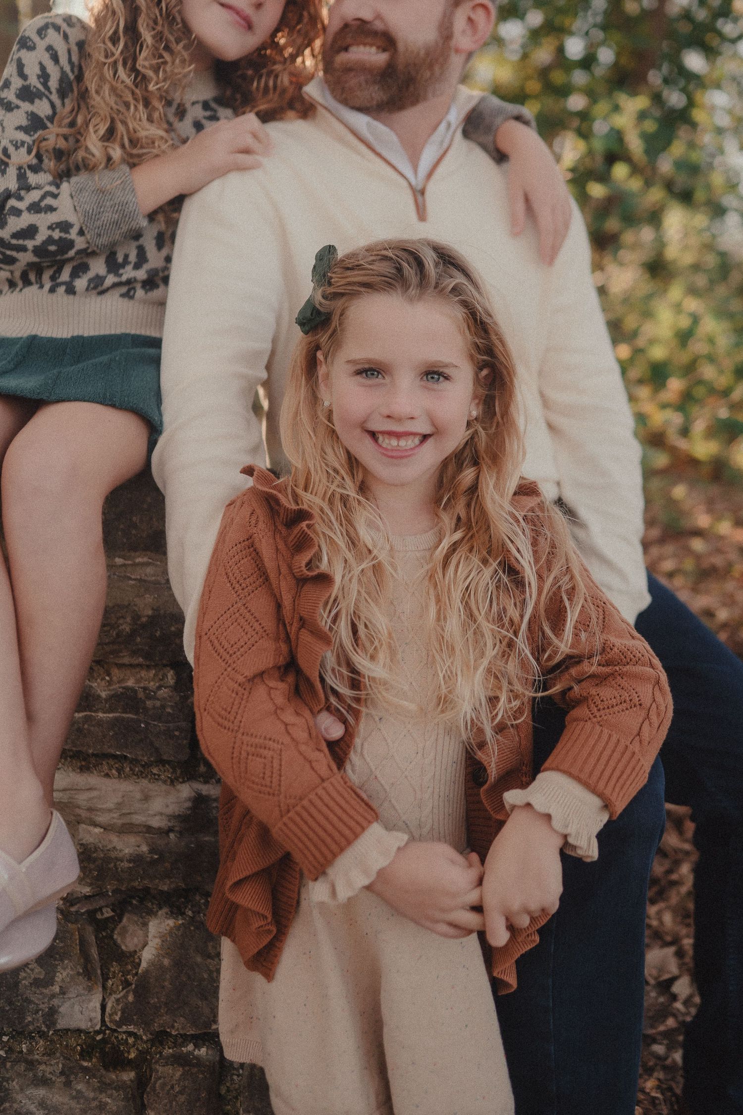 Warm autumn family portrait against stone wall backdrop with natural lighting.
