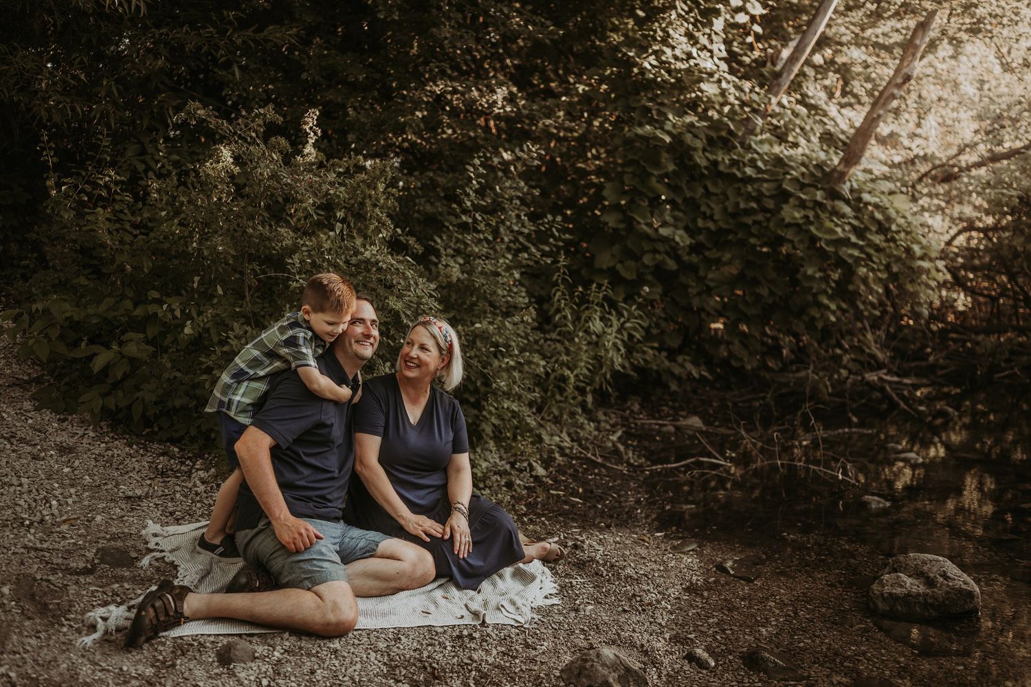 A couple sitting together on a rocky riverbank during golden hour.