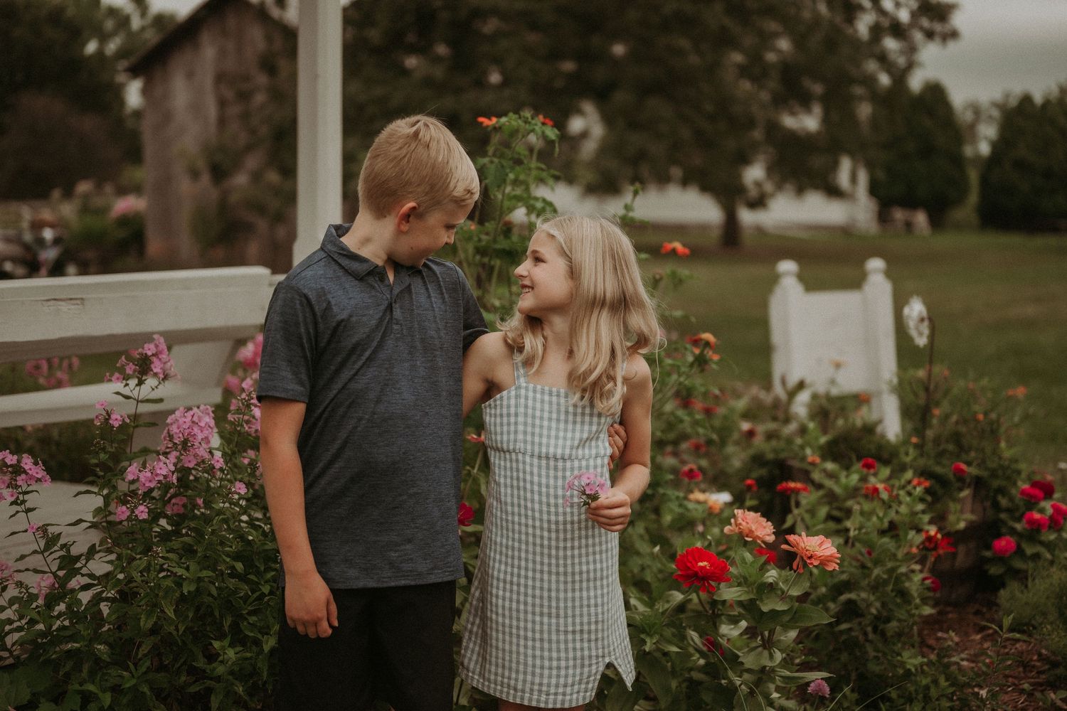 Children posing together near a blooming rose garden with white fence.