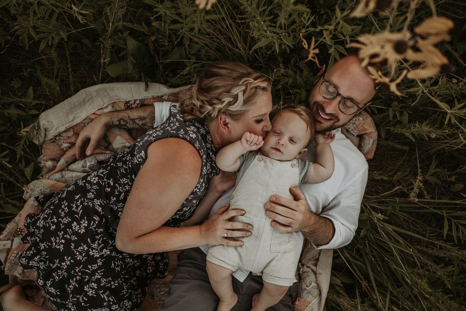 An intimate family moment captured lying in tall grass during golden hour.