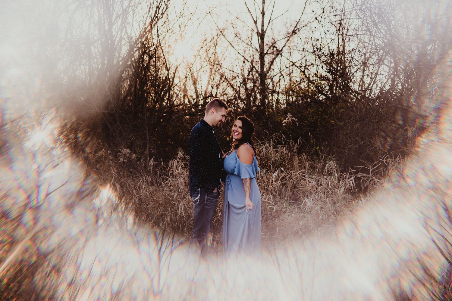 Artistic engagement photo with light leak effect showing couple in field at golden hour.