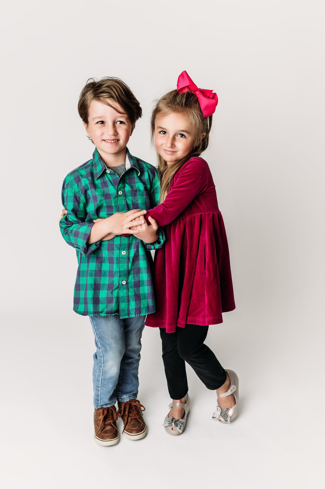 Two children in holiday attire stand together against white backdrop.
