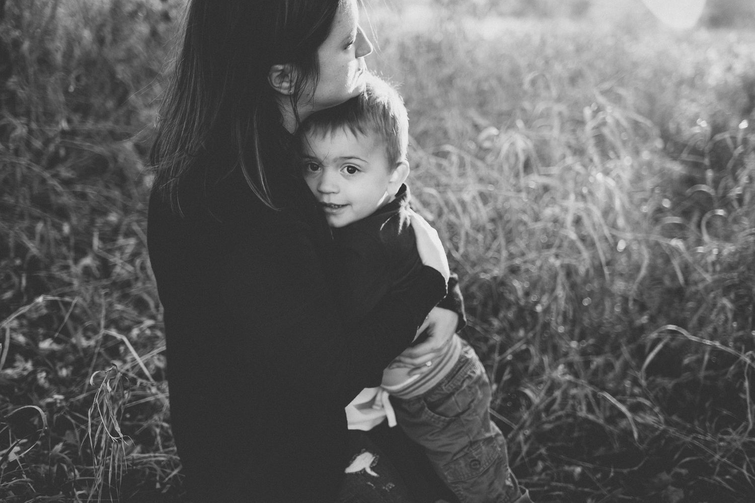 Black and white intimate portrait of parent and child in tall grass.