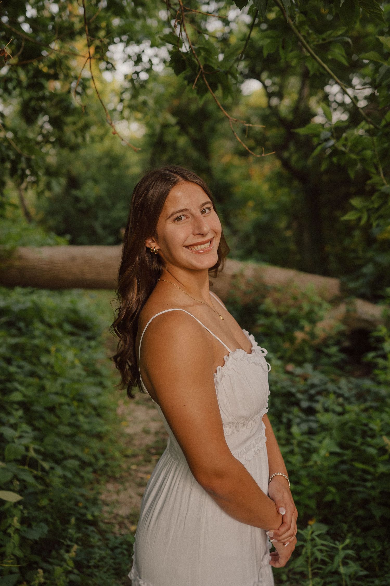 Summer portrait in white dress among green foliage with warm natural lighting.