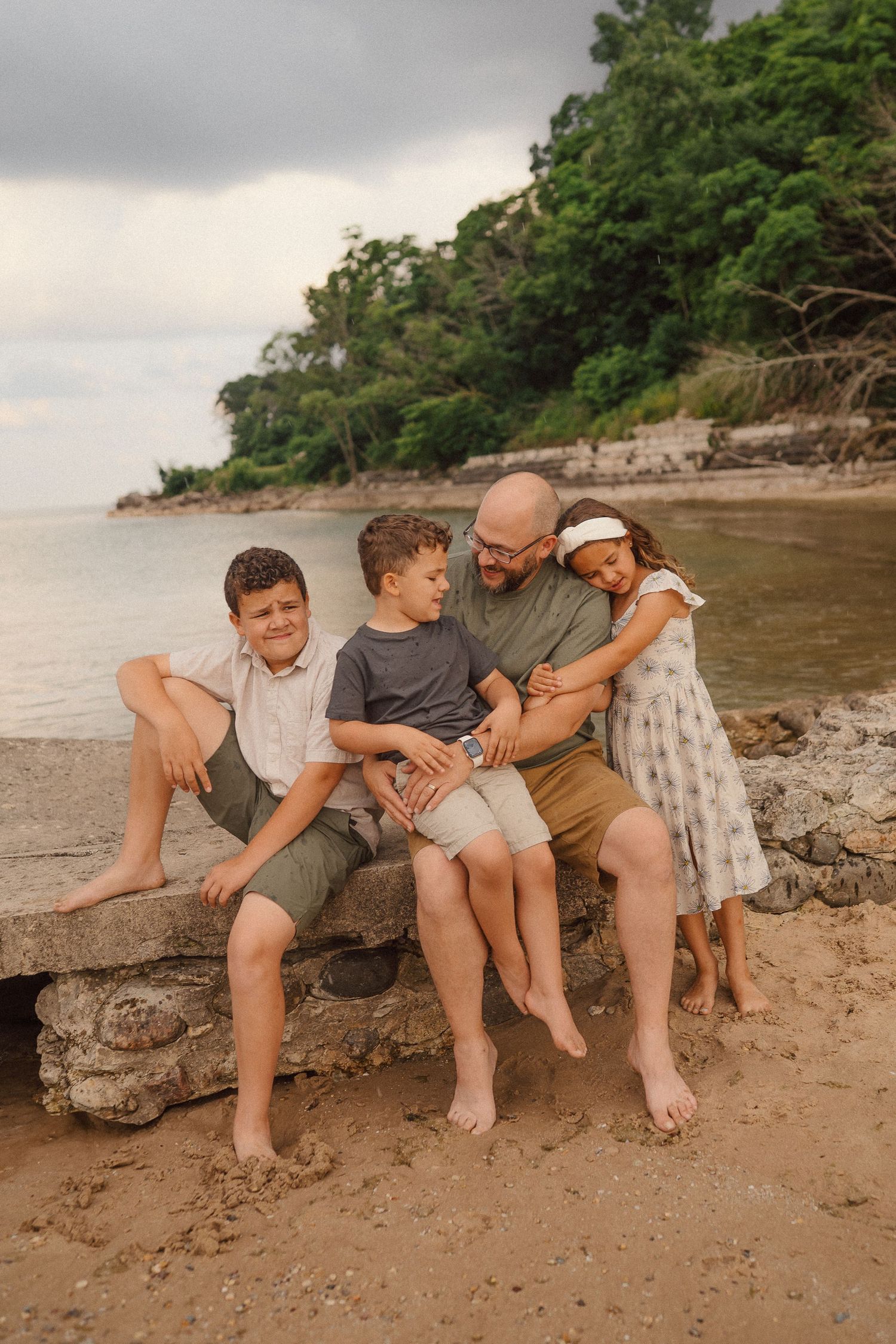 A family shares an intimate moment while sitting together on rocks at the beach.