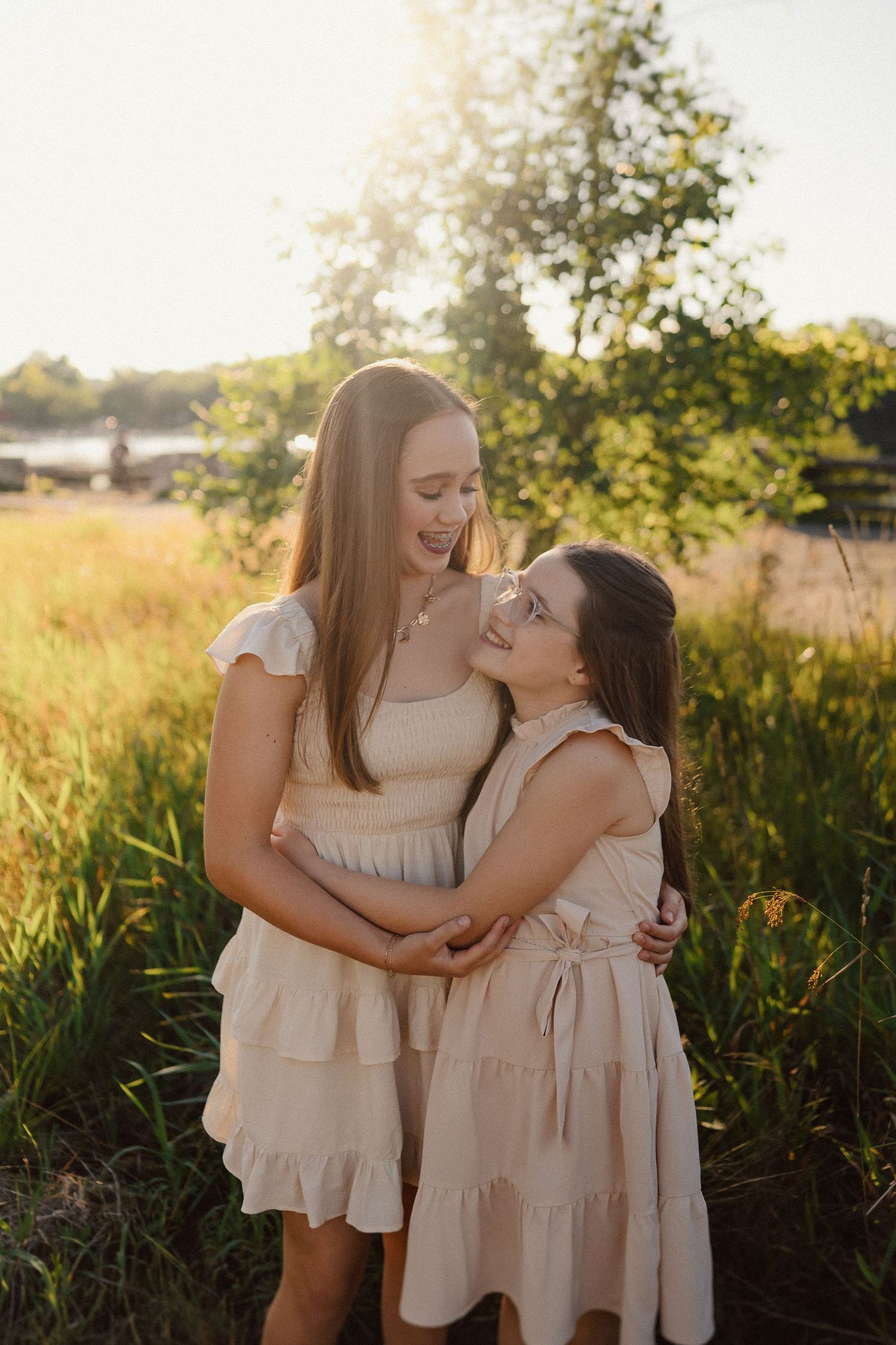 Family in matching cream dresses embrace joyfully in a sunlit field at golden hour.