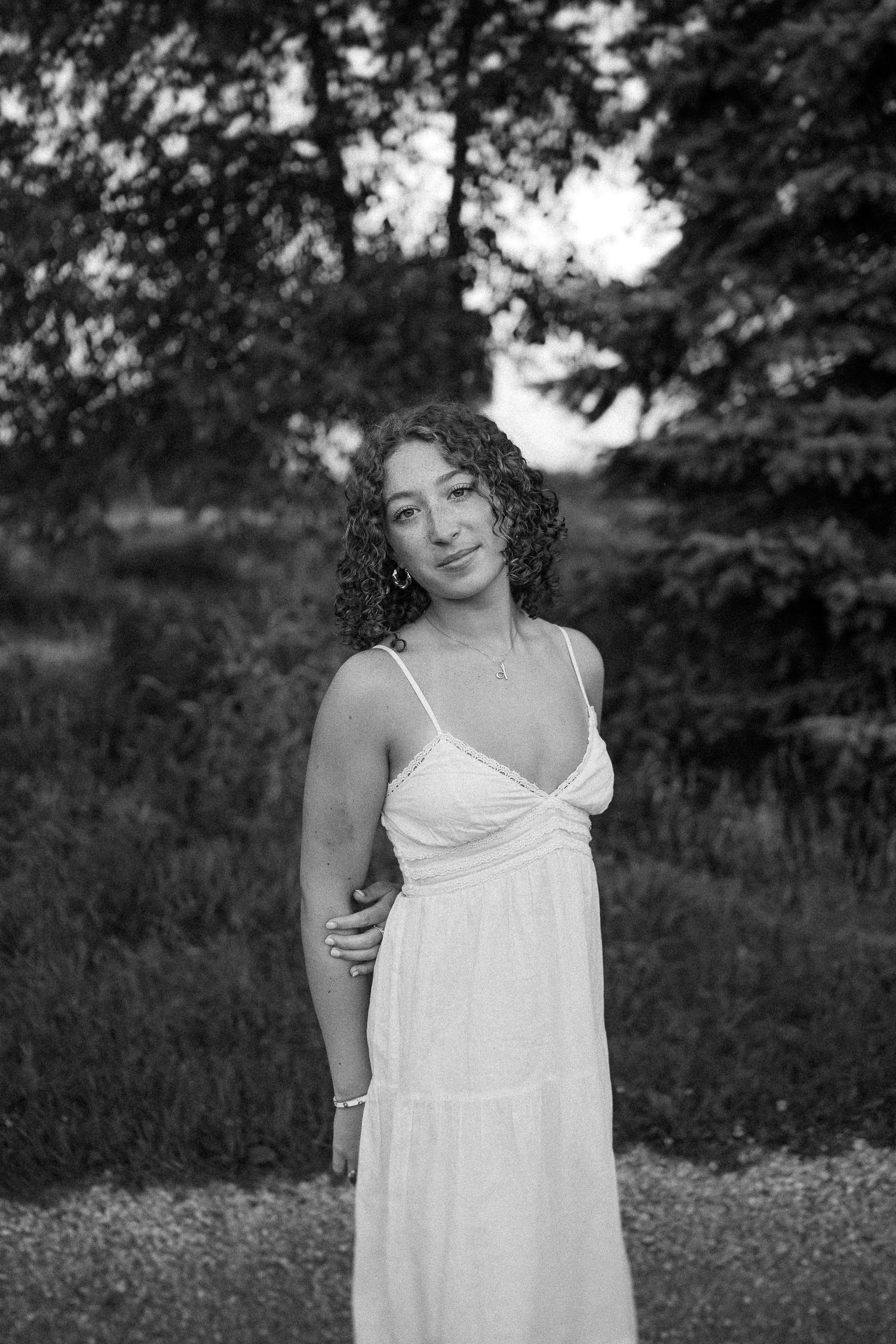 A series of black and white photos showing someone in a white sundress standing in a natural outdoor setting.