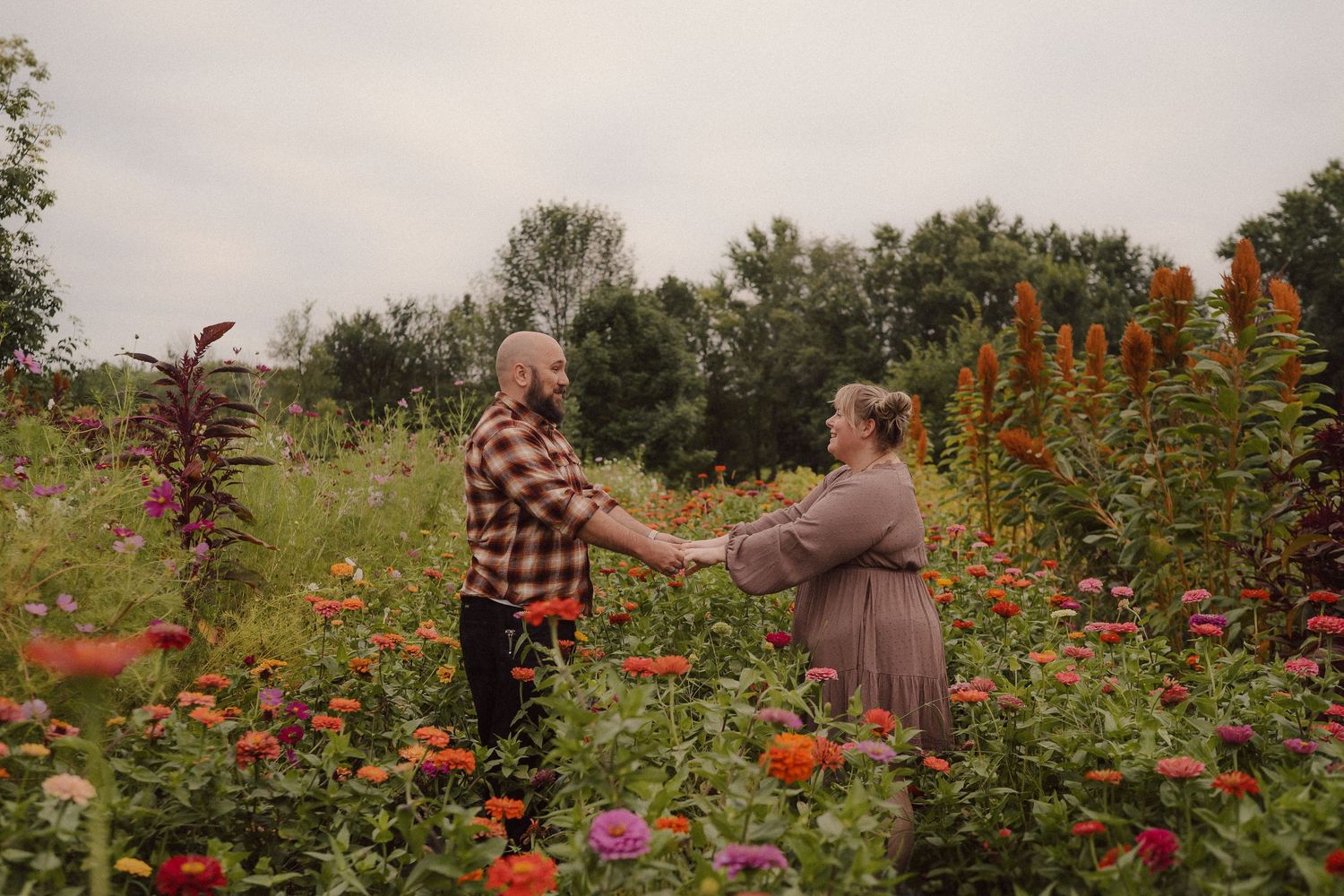 A couple walks hand in hand through a lush garden pathway surrounded by blooming flowers and greenery.