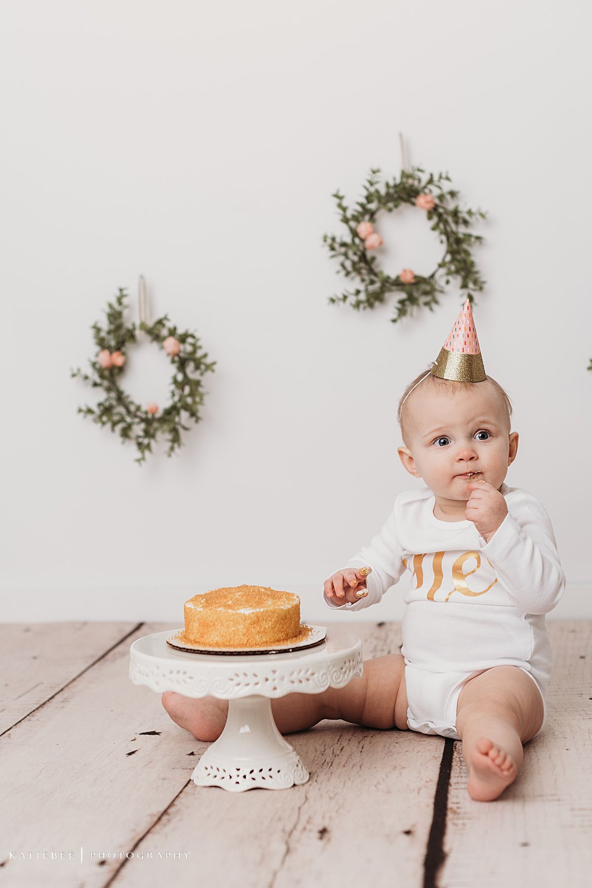 Close up of baby's hand reaching towards cake on white wooden surface.