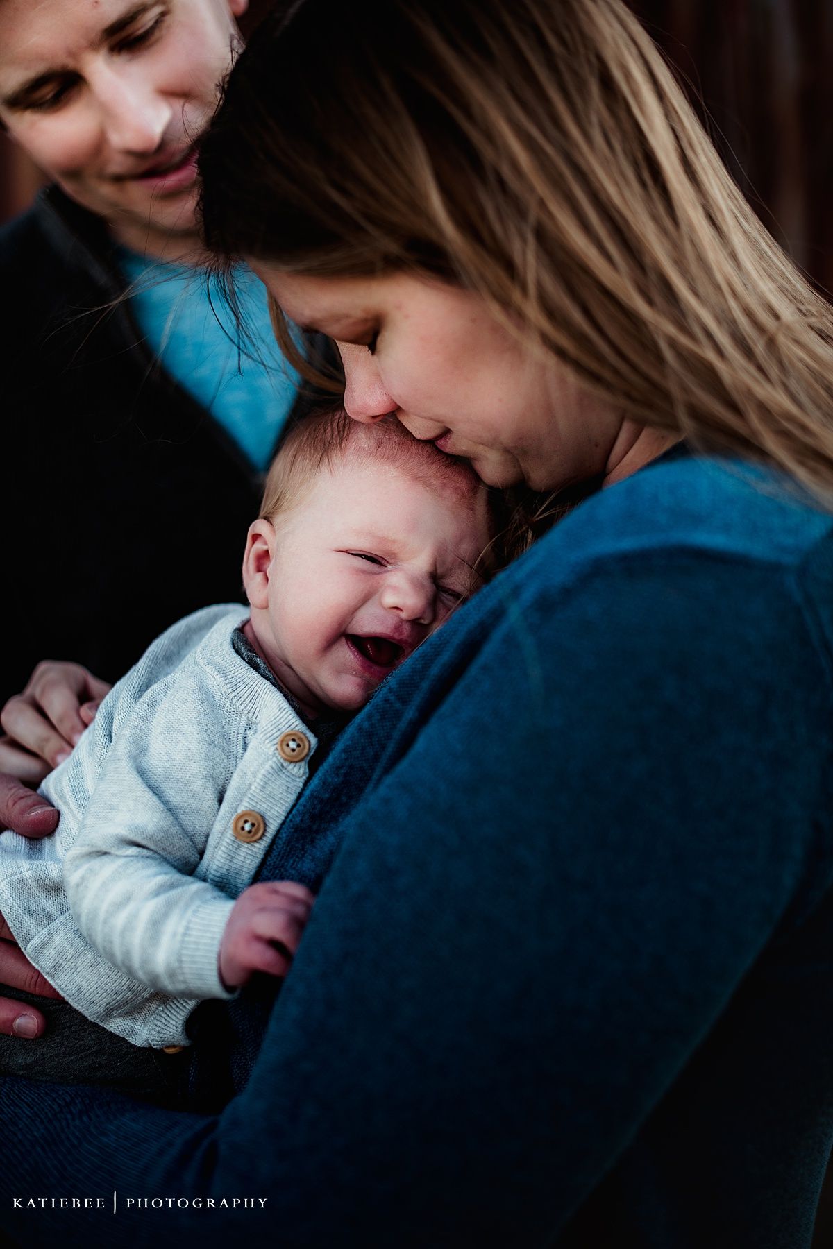 Tender family moment with baby laughing against dark background.
