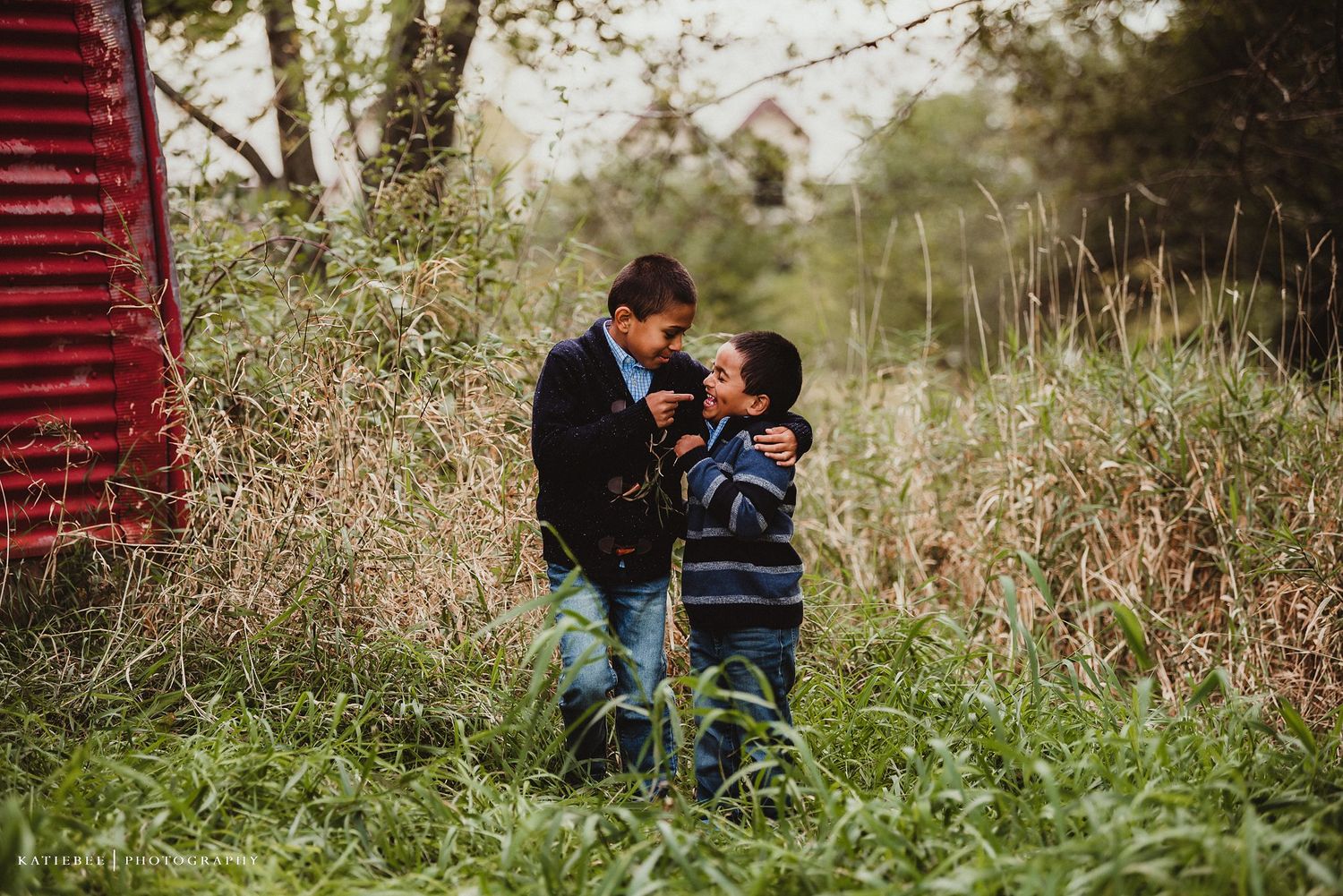 Candid moment of two people walking through tall grass near red barn.