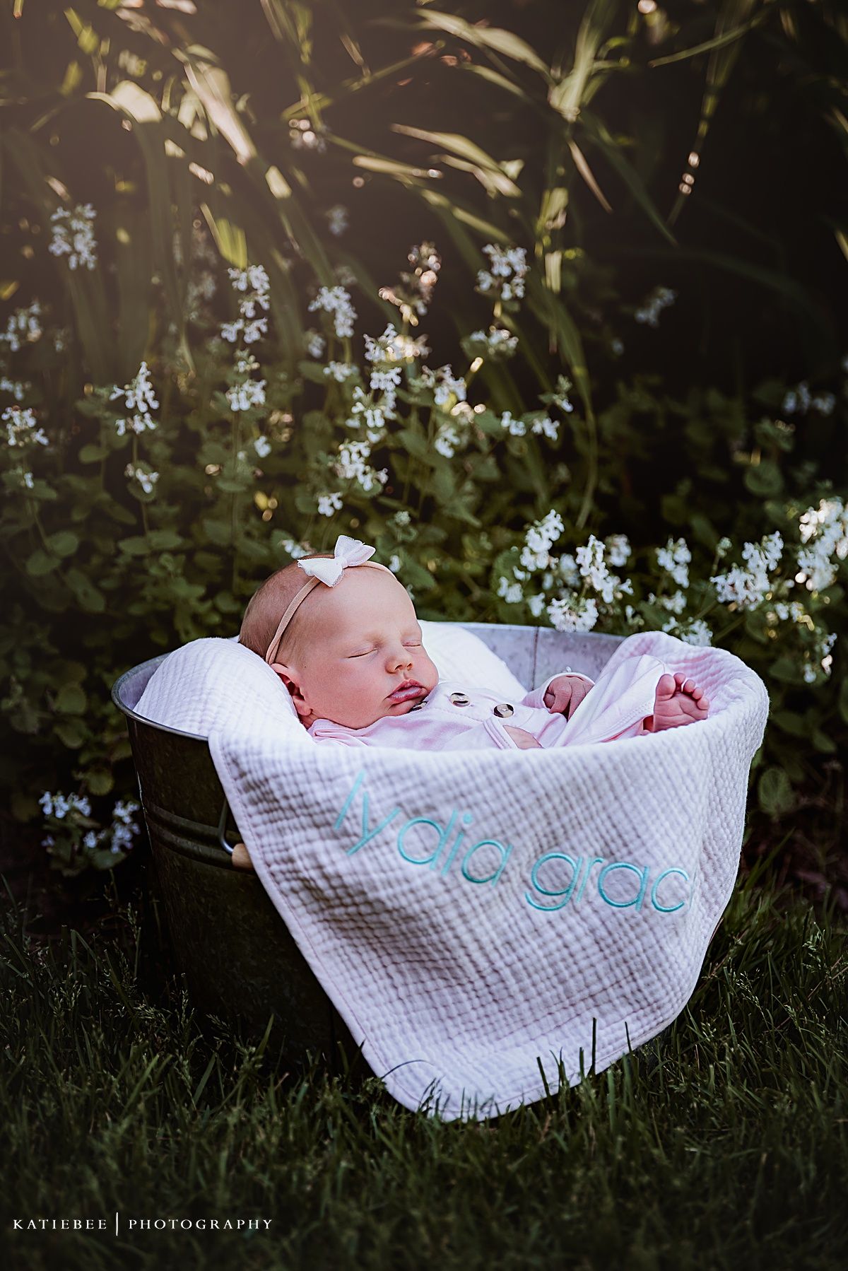 Sleeping newborn wrapped in white blanket outdoors among delicate blue flowers.