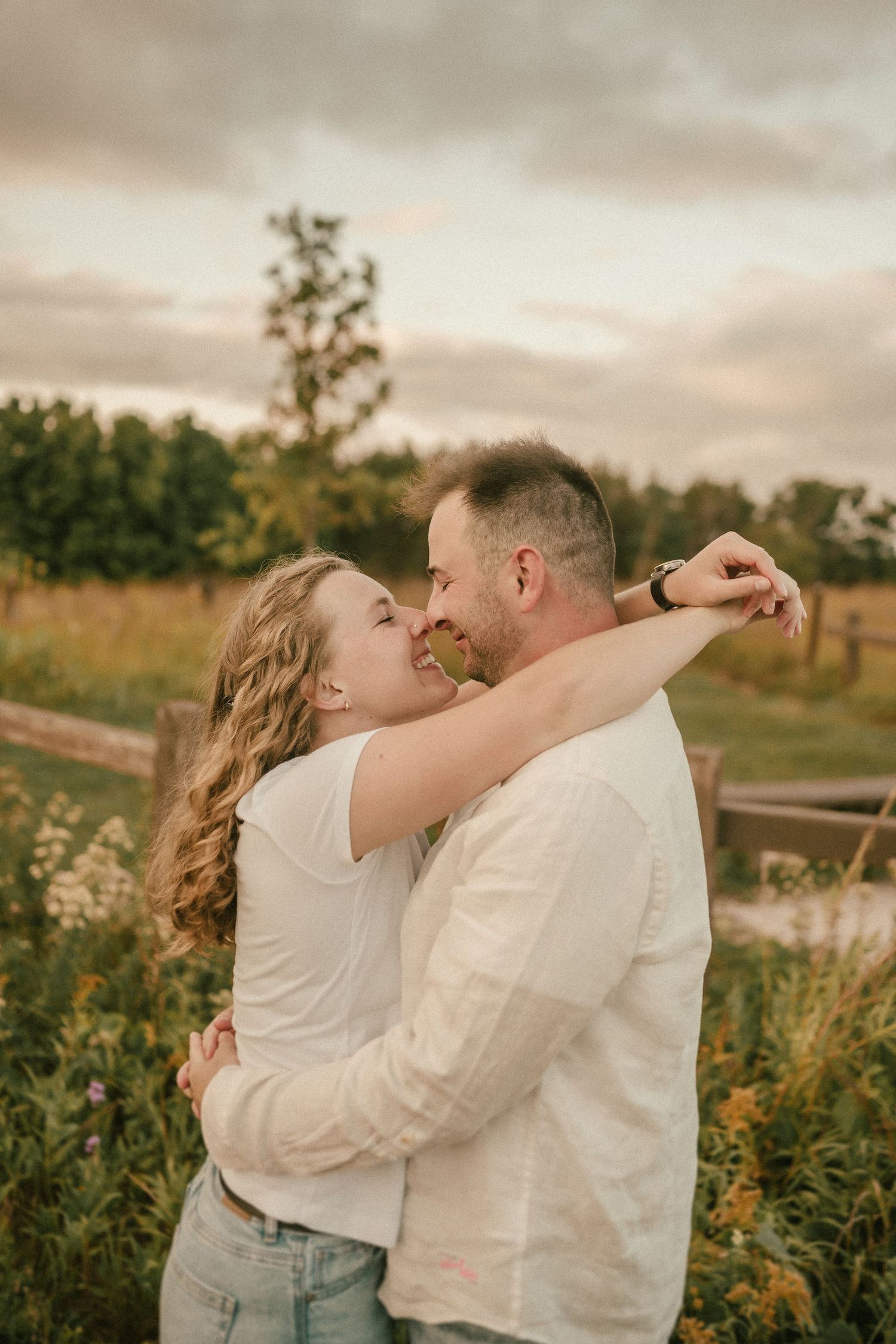 A couple embraces lovingly in a wildflower field during golden hour.