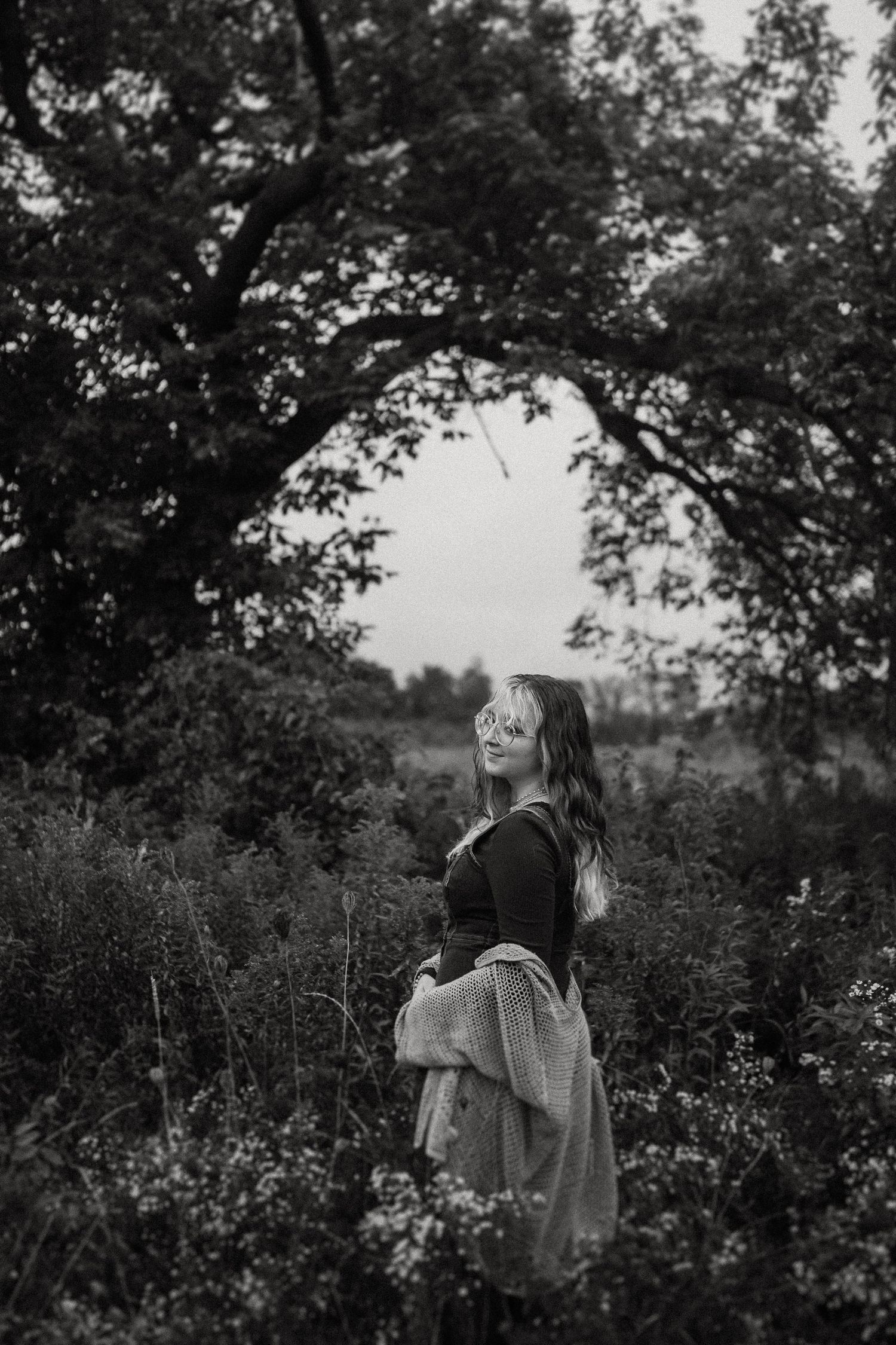 Black and white outdoor portrait showing someone in a field with trees and natural scenery.