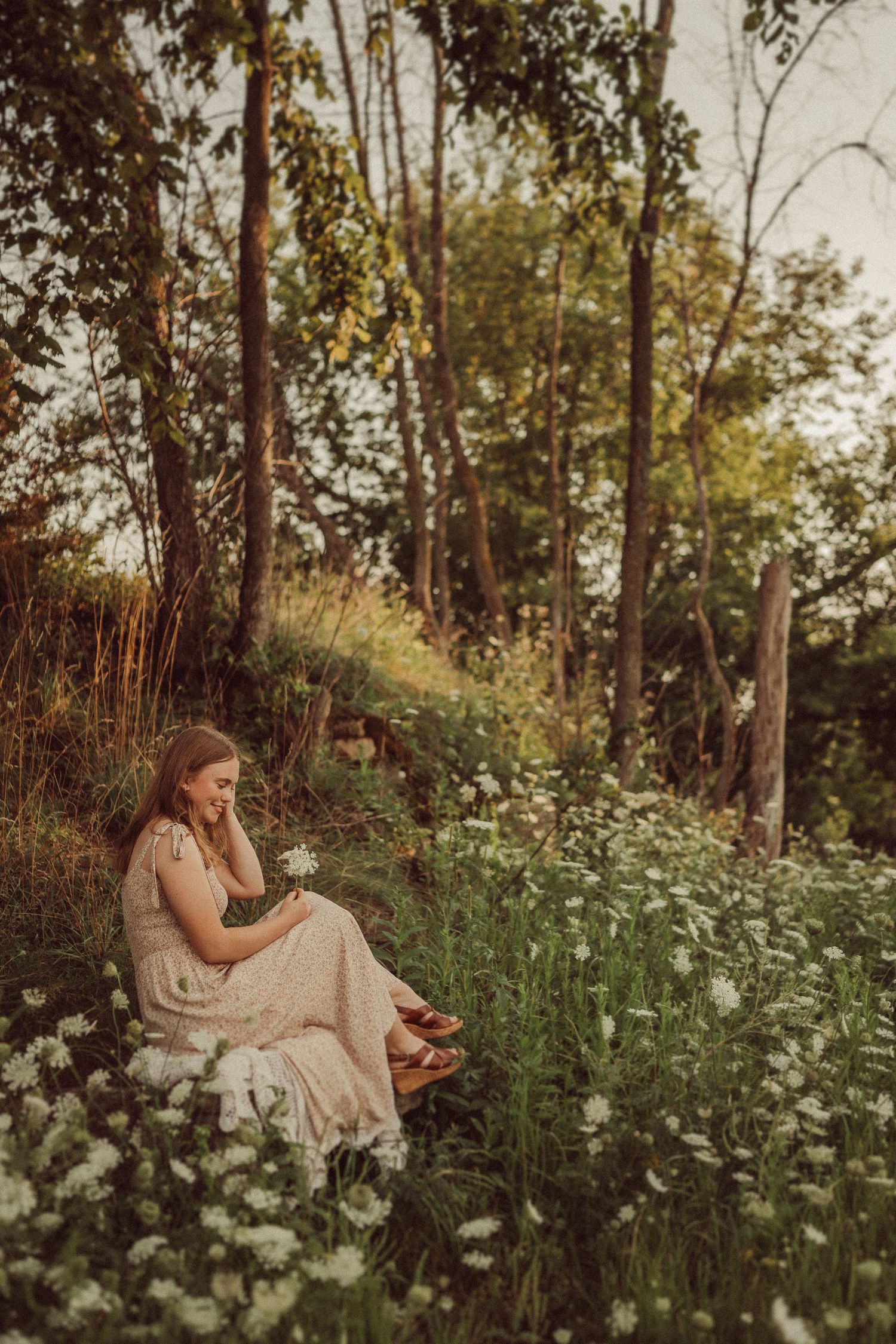 An ethereal sunset portrait in a wildflower meadow with soft golden lighting and forest backdrop.