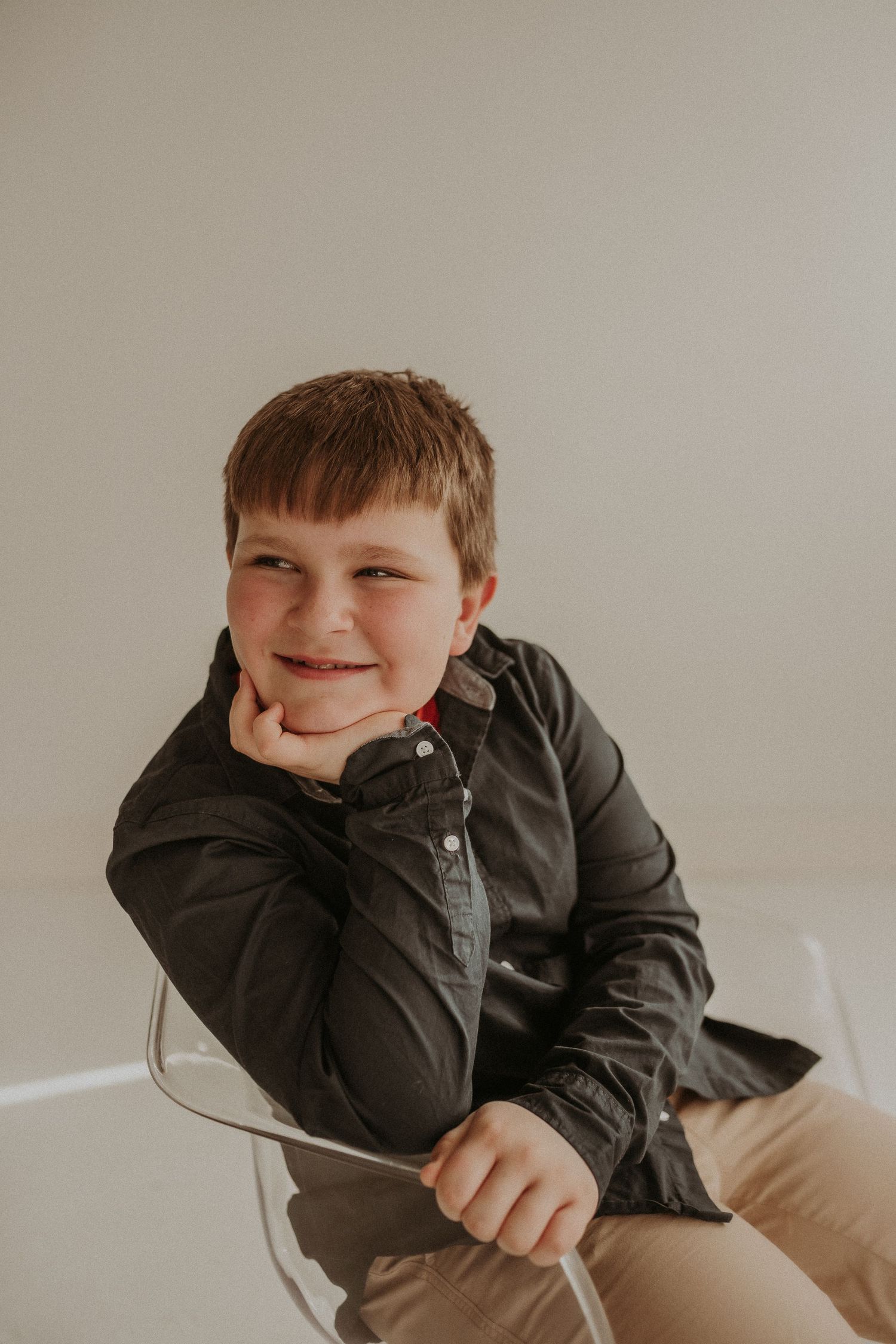A cheerful pose with hand resting on chin while seated in a modern white chair.
