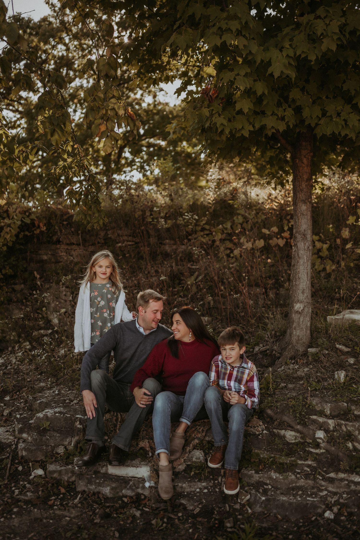 Family sitting together on stone steps during golden hour in an autumn forest setting.