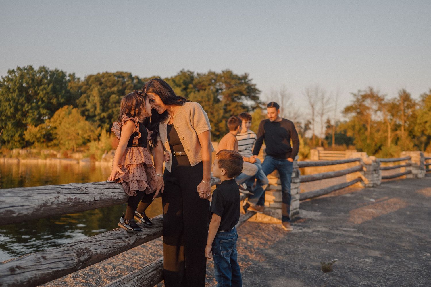 A group walks along a rocky beach shoreline at sunset with water and reeds in the background.