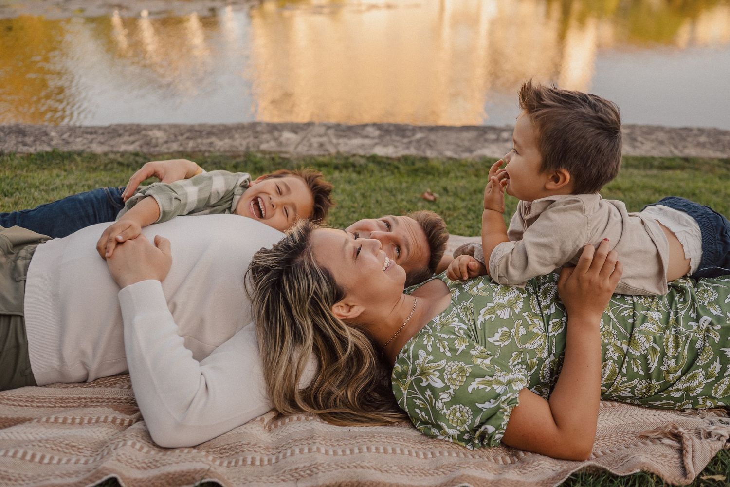 Family lying together on grass during golden hour by the water.