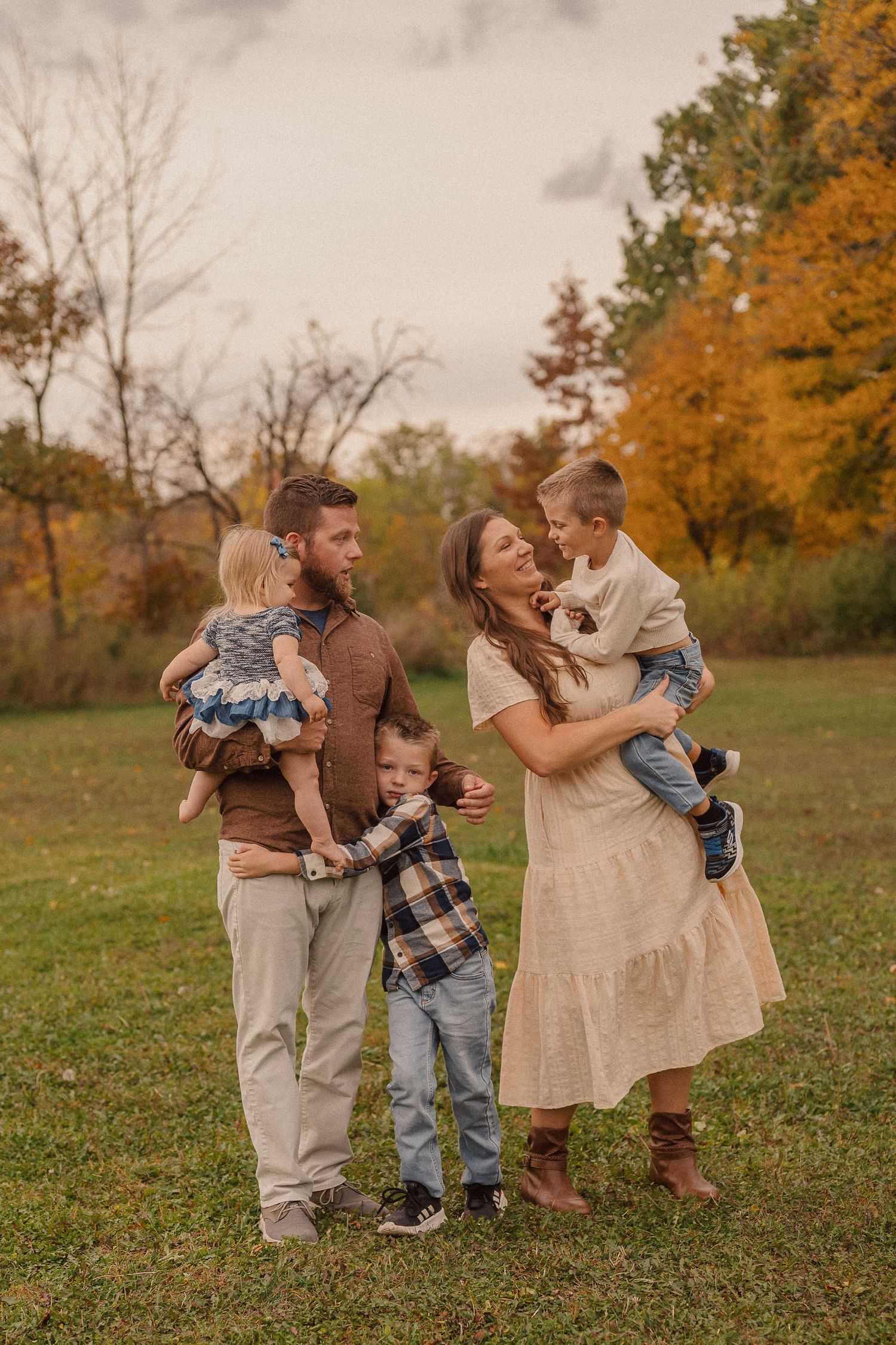 A candid family moment captured in a grassy field with autumn trees in the background.