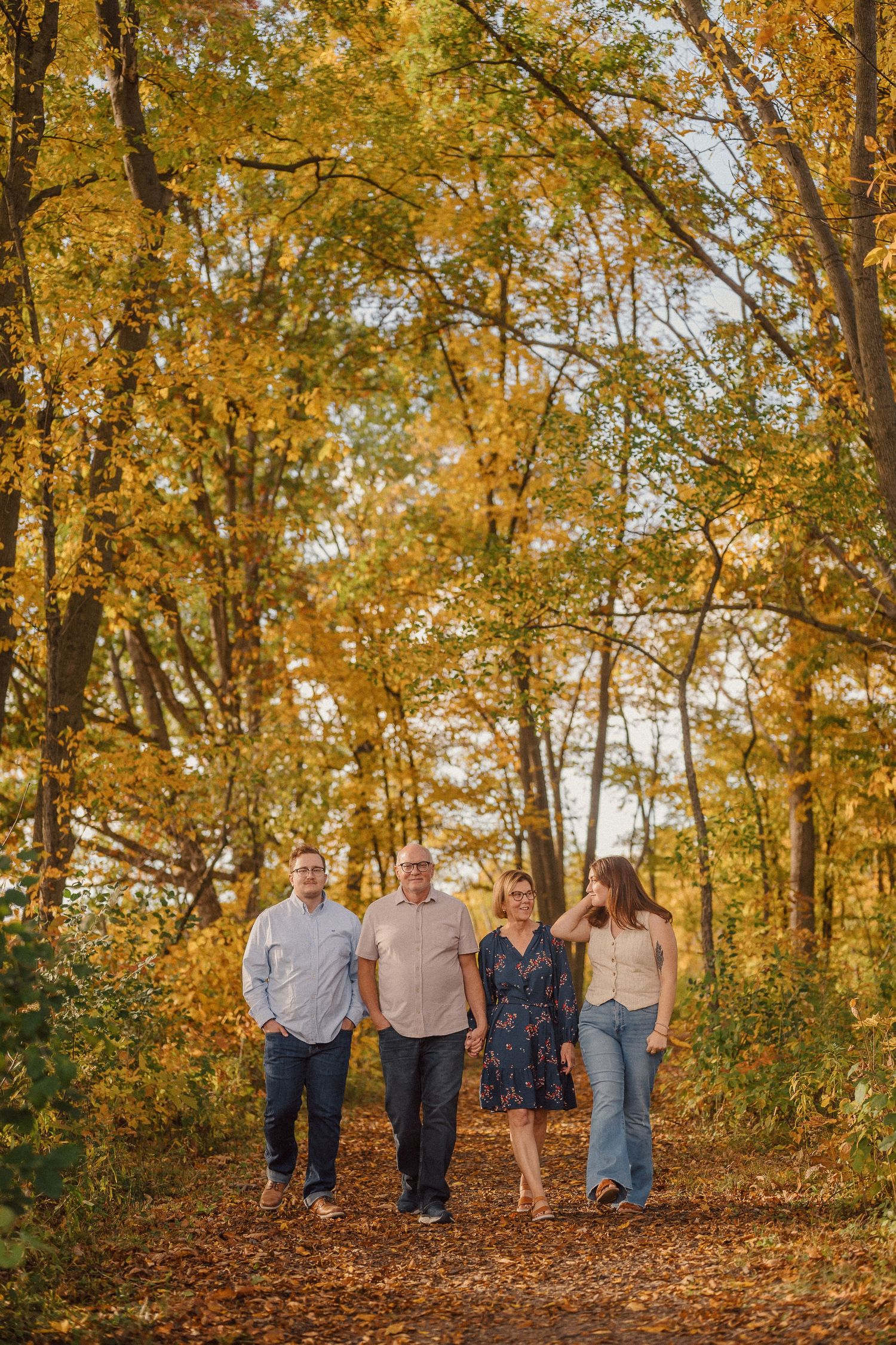 A group walks together on a leaf-covered path through vibrant autumn trees with golden foliage.