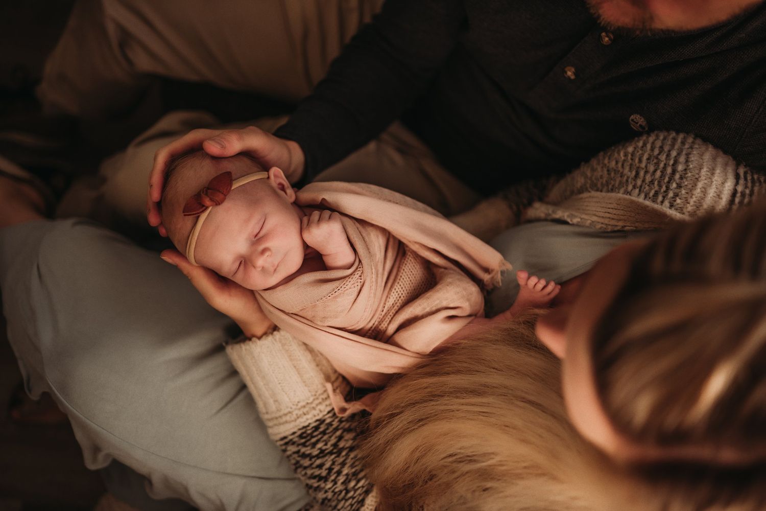 A sleeping newborn baby wrapped in a tan swaddle blanket on a couch.