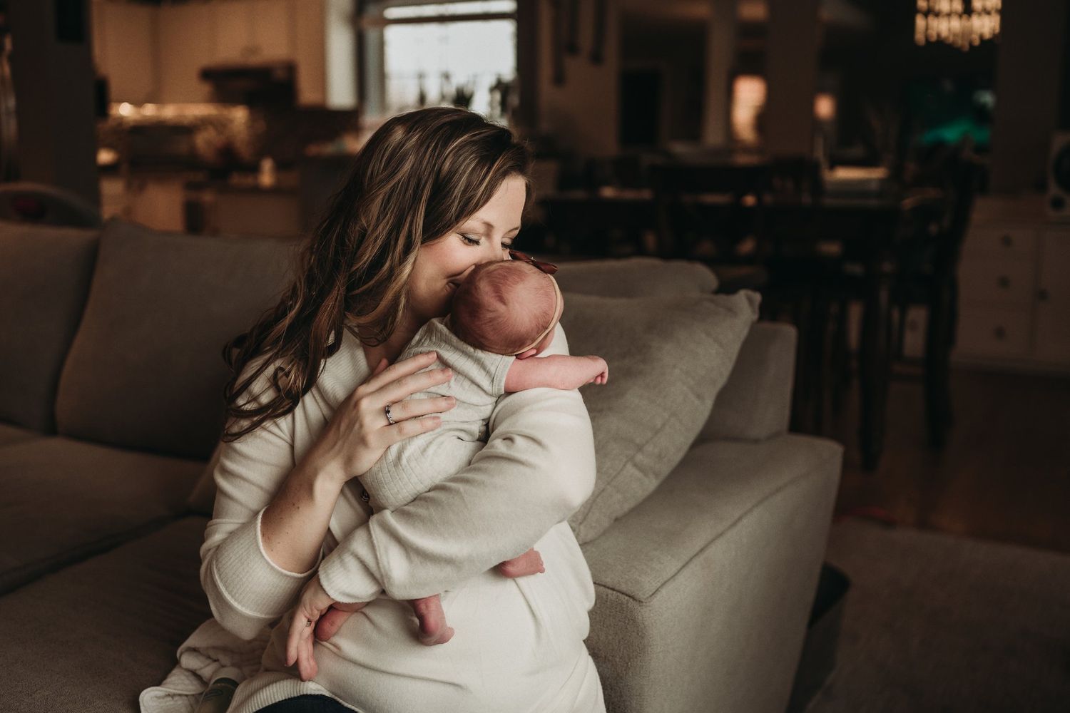 Intimate moment of parent holding sleeping infant on grey couch.