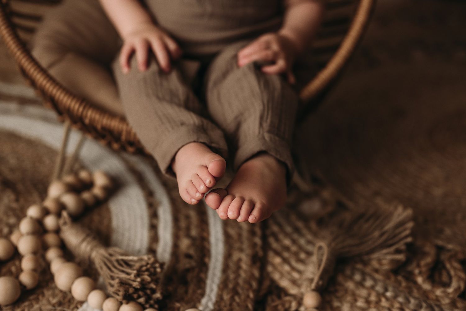 Close-up of tiny feet and wooden beads on a textured carpet with neutral tones.
