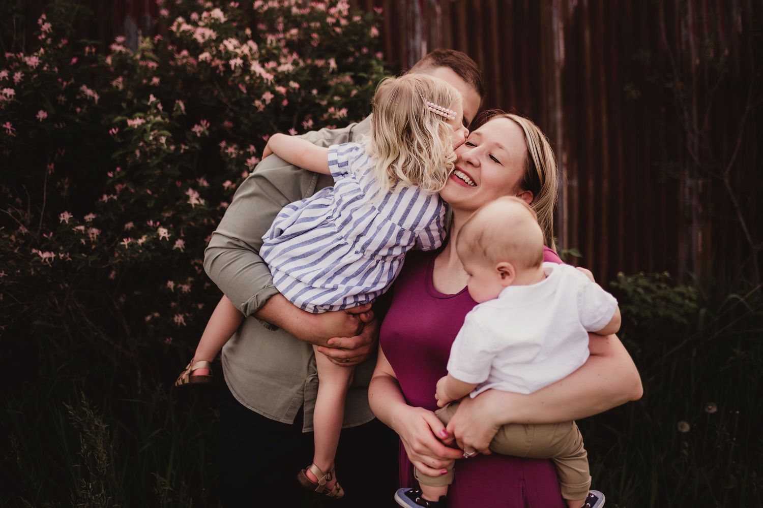 Joyful outdoor family portrait with children against a rustic barn backdrop.