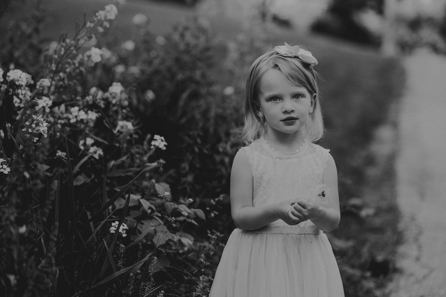 Monochrome image of a child standing near blooming flowers in a garden setting.