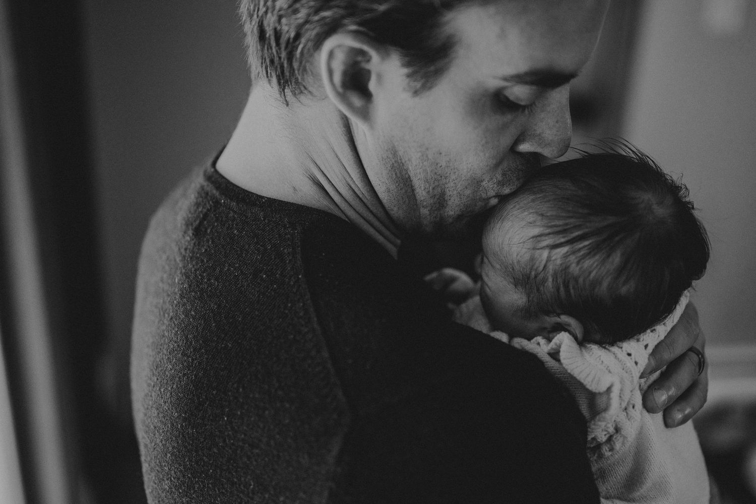 A tender moment between parent and newborn baby in black and white photography.