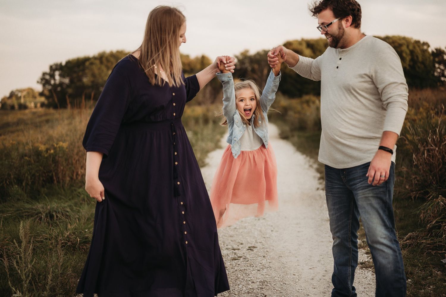 Three people hold hands while walking down a path during golden hour.