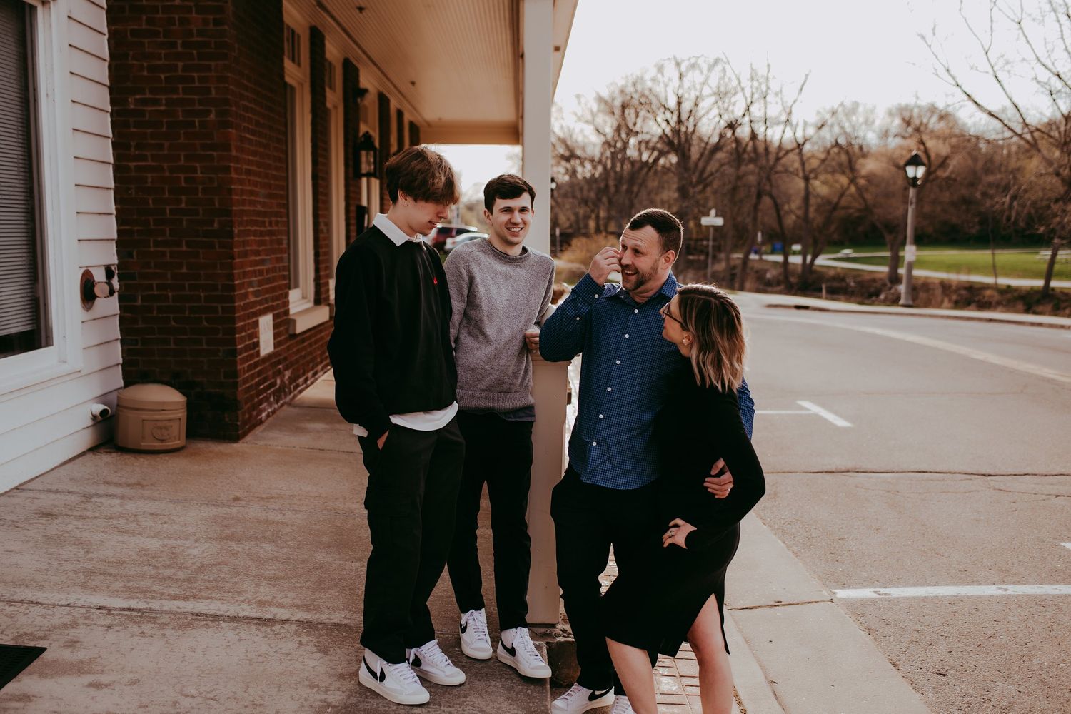 Four people laughing and sharing a casual moment outside a brick building.