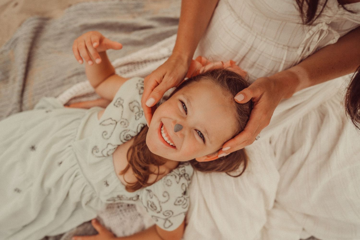 Joyful moment of tender childhood play as someone rests on soft white bedding.