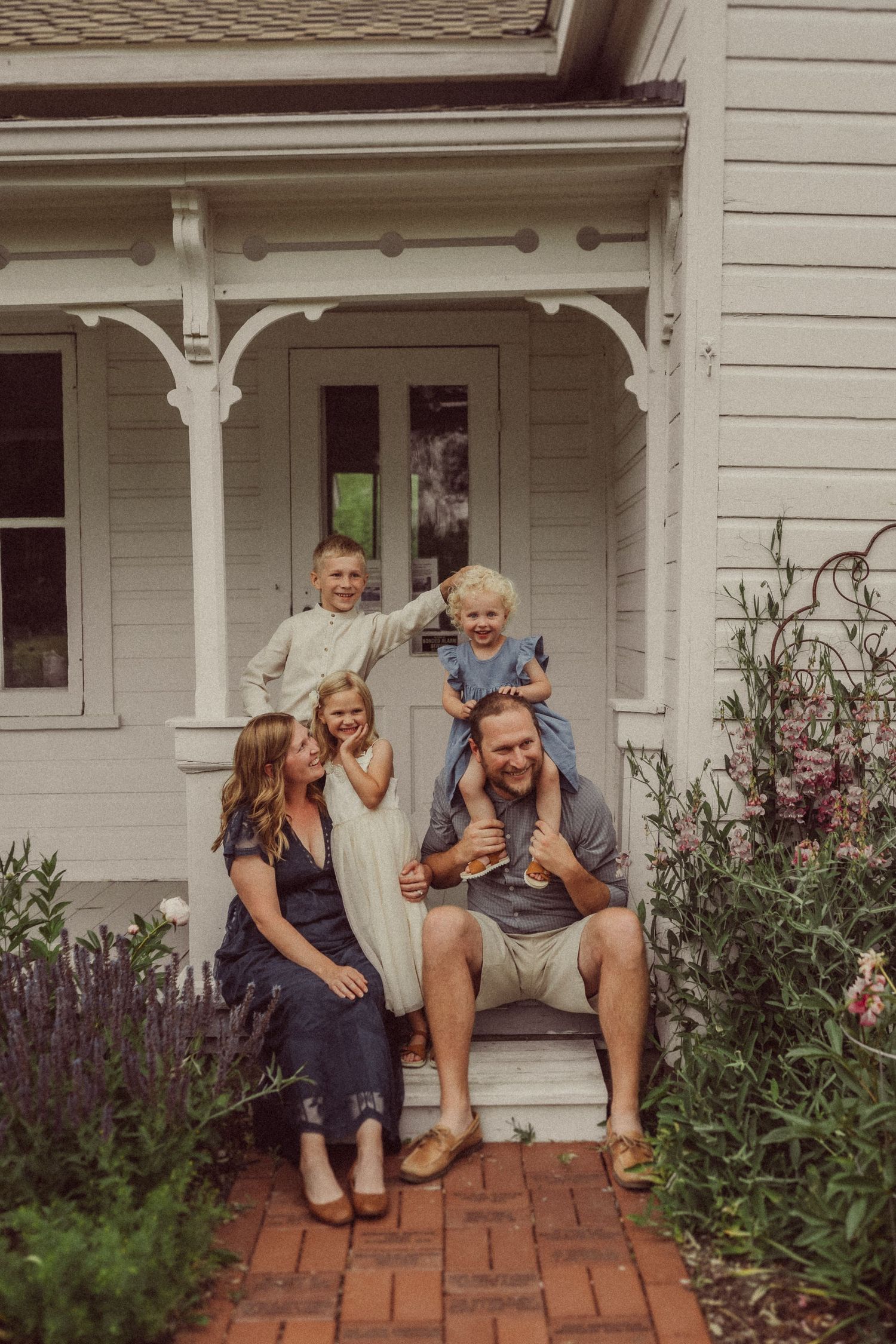 Playful family portrait on farmhouse porch steps surrounded by purple lavender and summer blooms.