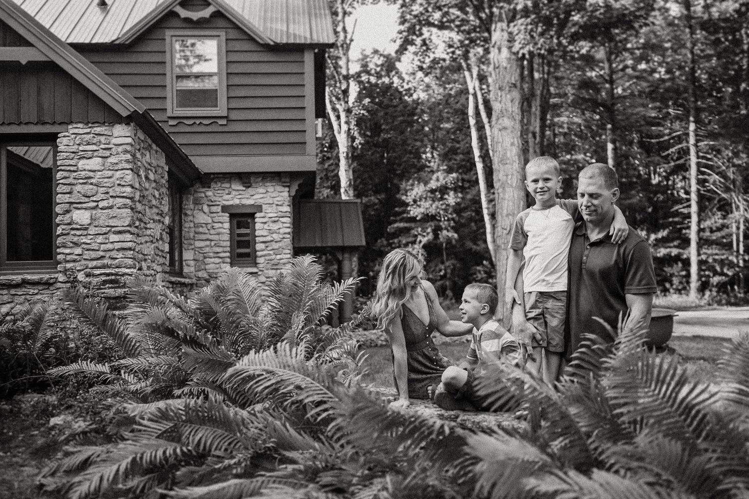 Black and white photo of family gathered by stone wall surrounded by ferns.