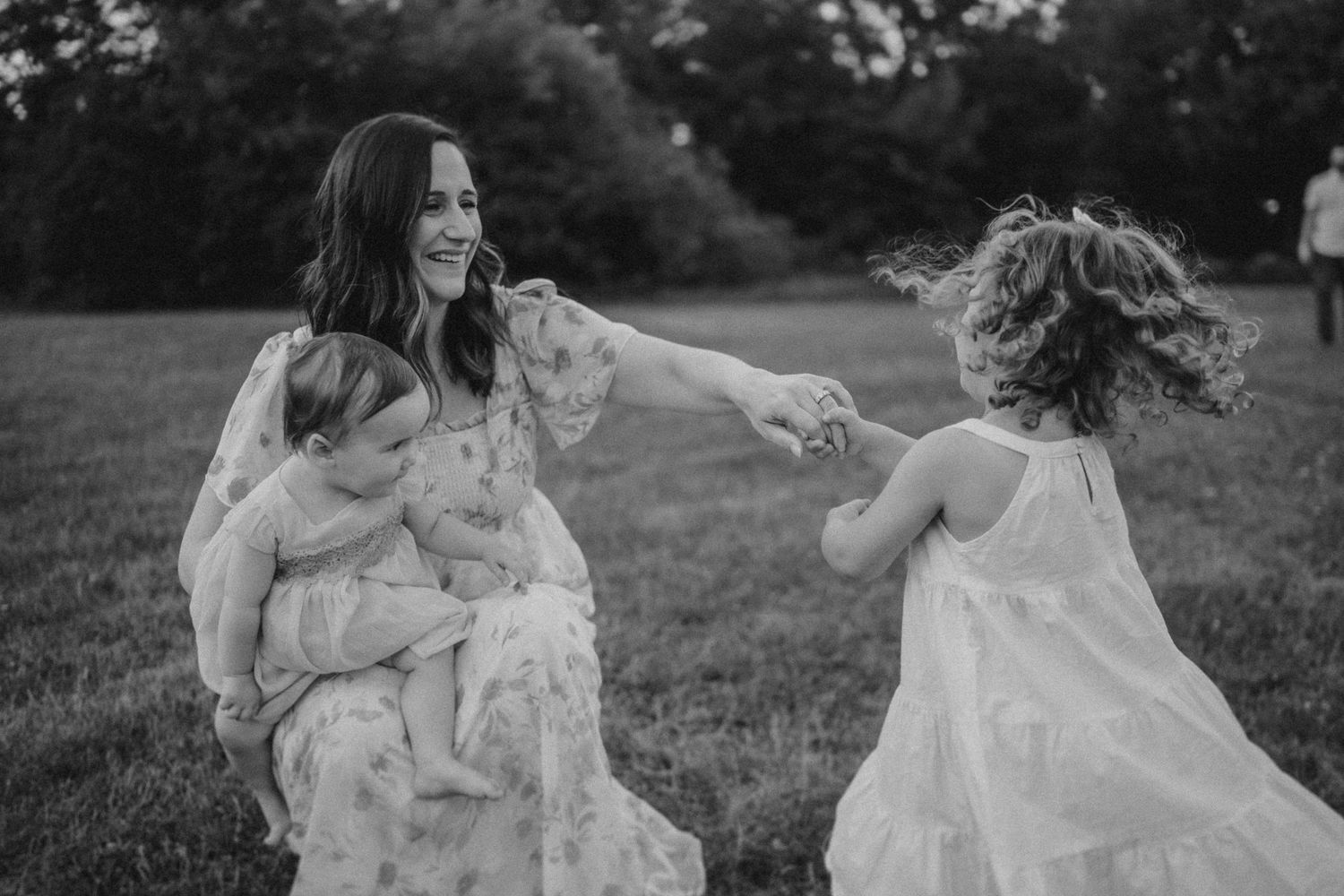A candid black and white photograph capturing playful family moments in a grassy field.