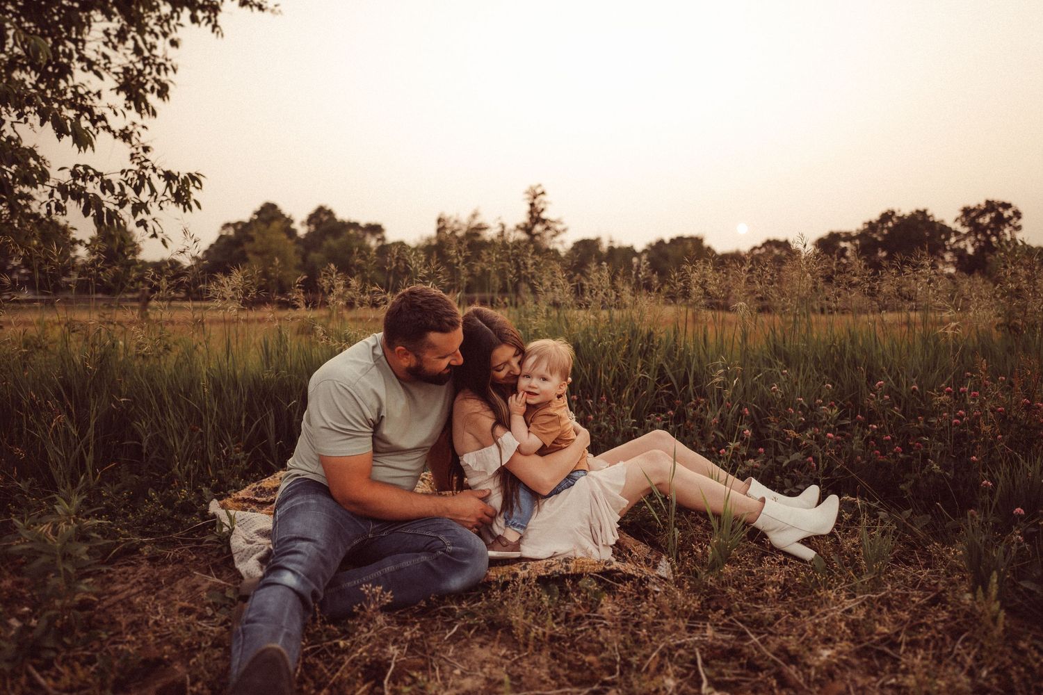Intimate family portrait captured in a golden field during sunset.