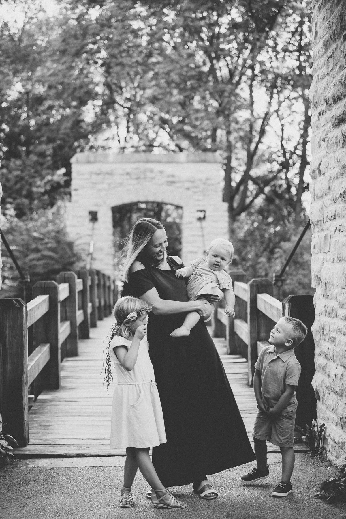 A black and white family portrait on a wooden bridge with stone architecture.