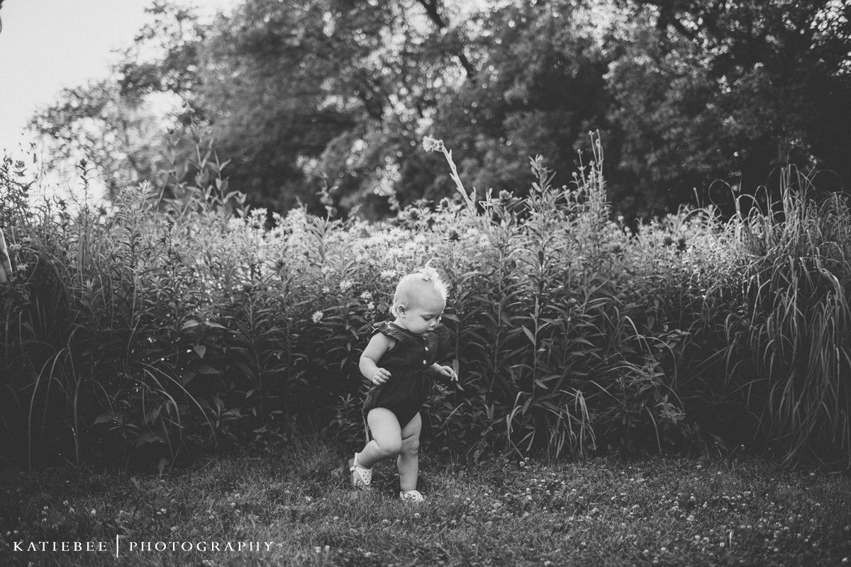 Black and white portrait of a toddler standing in tall grass at sunset.