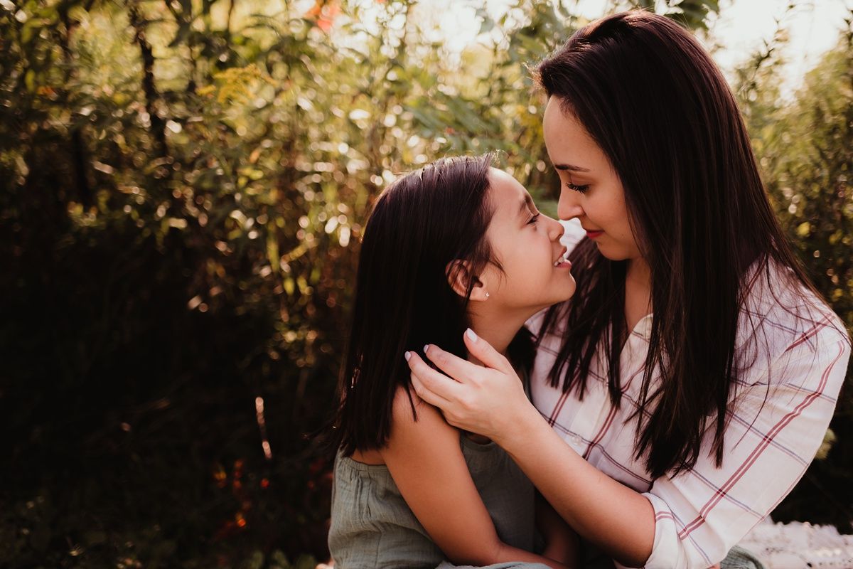 Two people sharing an intimate close-up moment outdoors against natural foliage.