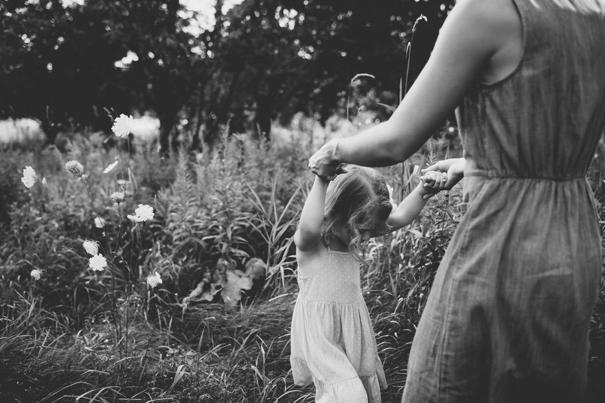 A black and white image showing parent and child walking through wildflowers.